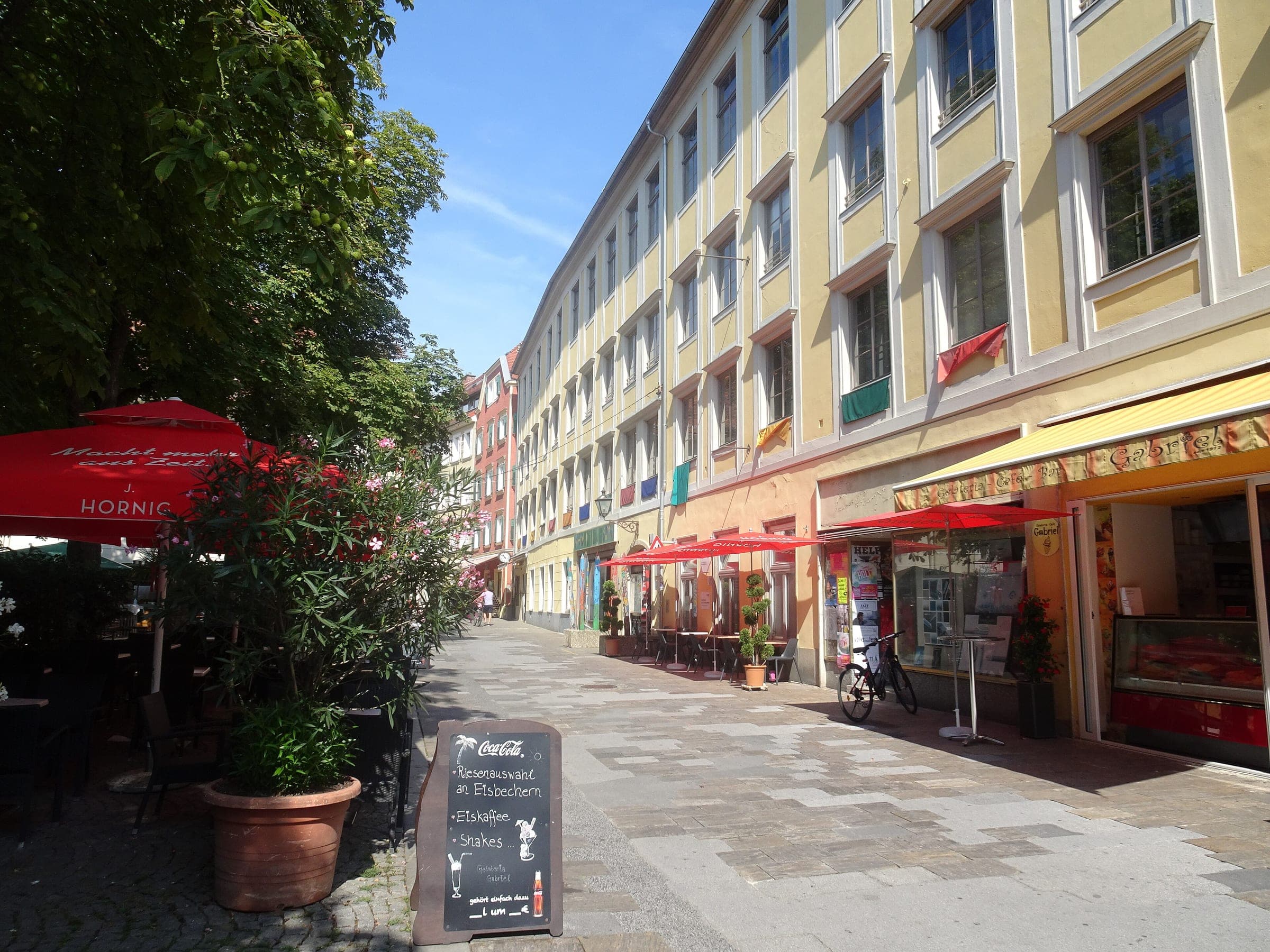 Café umbrellas and pale yellow facades line Färbergasse on its way into Färberplatz in Graz.