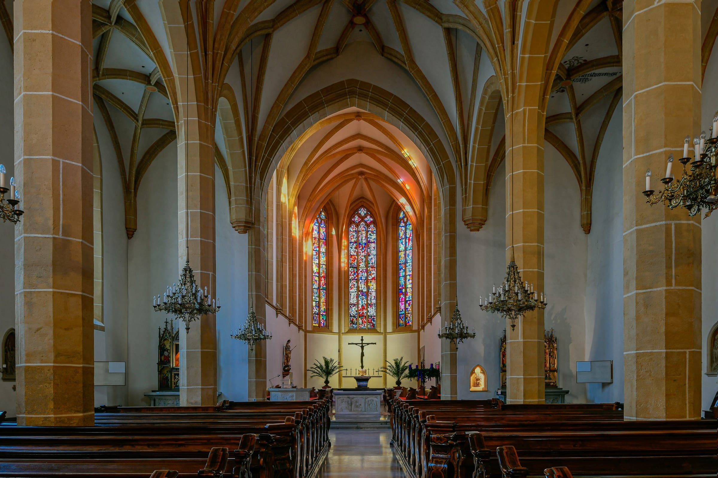 Chandeliers hang between the stone pillars of the Franziskanerkirche nave in Graz.