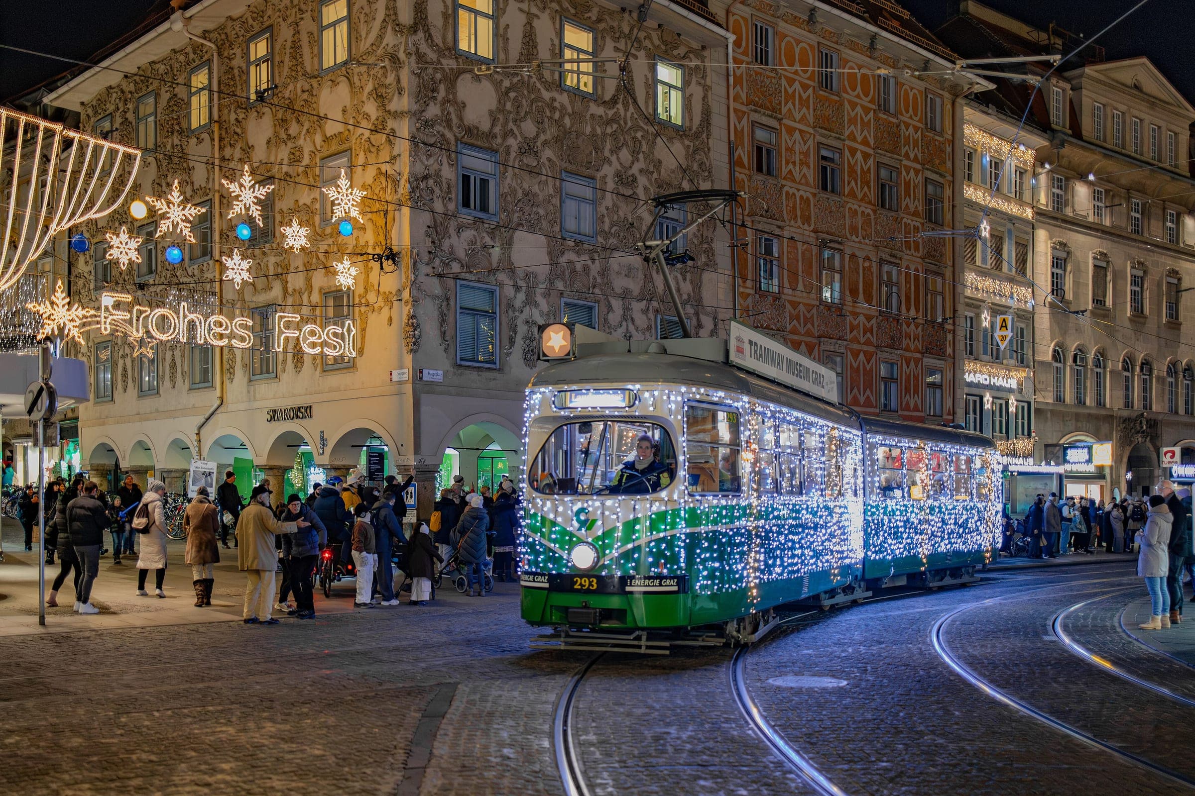 A tram wrapped in lights rolls across Hauptplatz in Graz past the Advent crowd and the stuccoed Luegg houses.