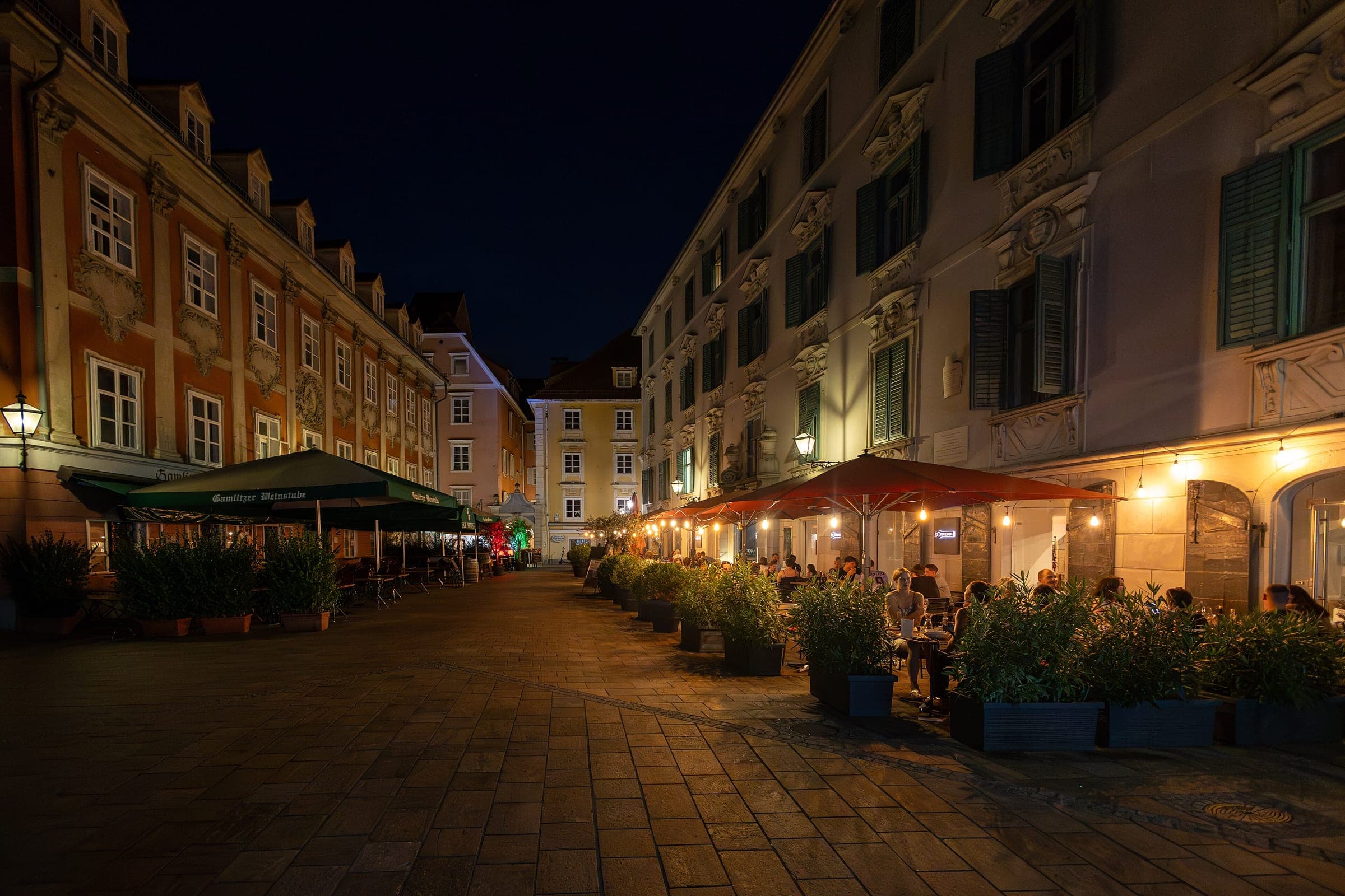 Lamps light the baroque facades and café terraces around the Mehlplatz in Graz at night.
