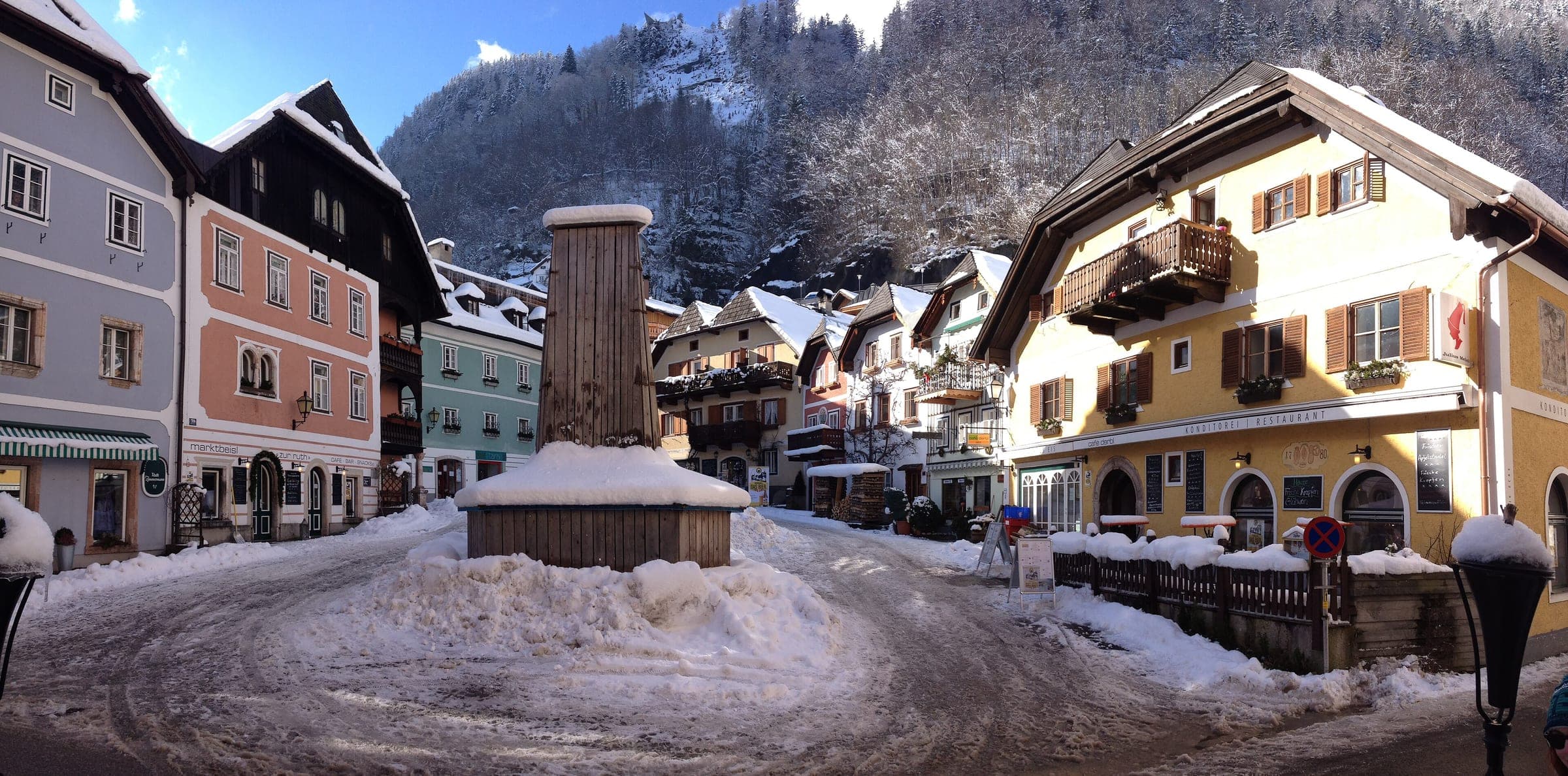 Snow is banked around the Trinity Column on Hallstatt's Marktplatz between painted houses