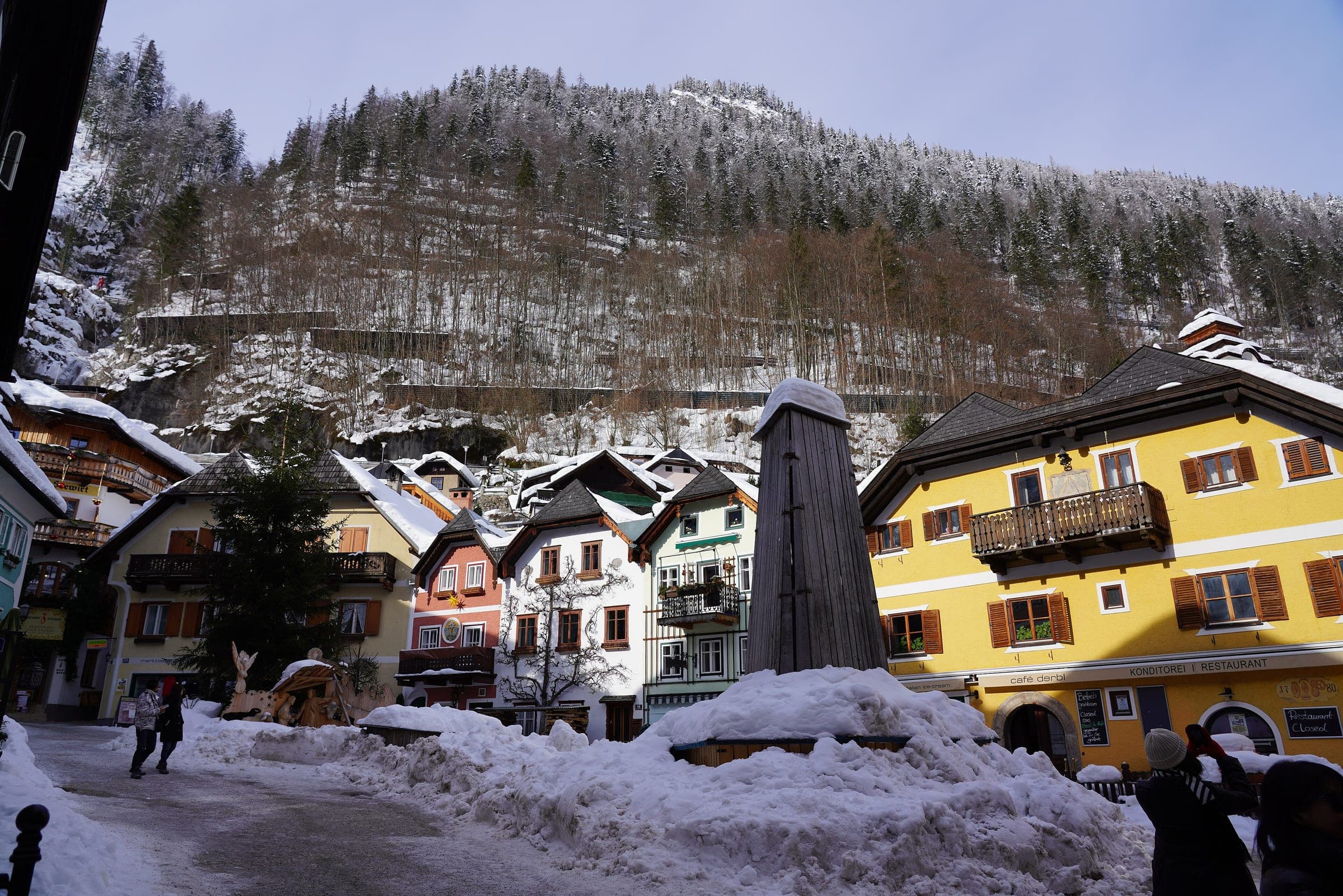 Snowy forest climbs above the yellow and timber houses of Hallstatt's Marktplatz in January