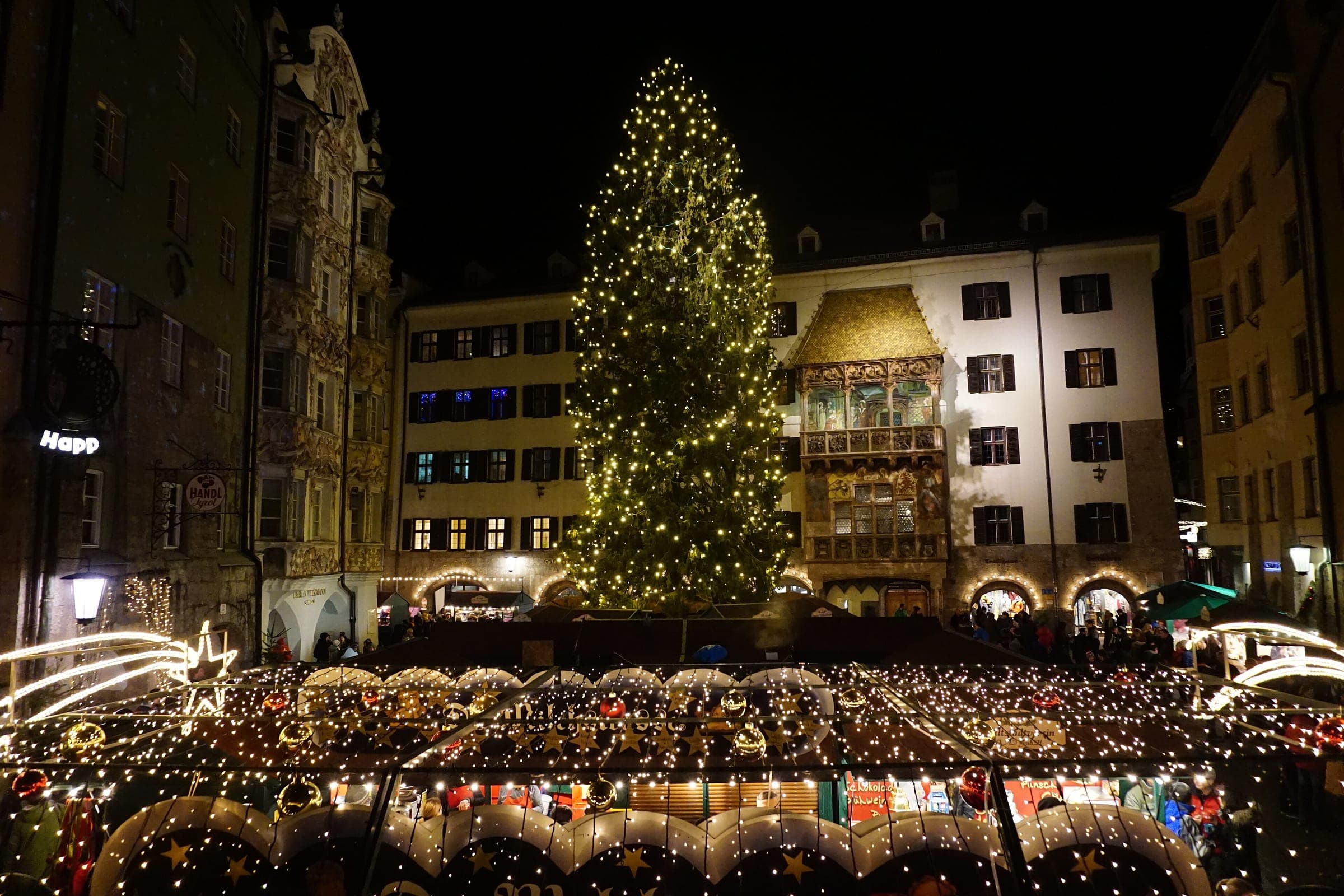 The Christmas tree and lit stall roofs fill the square in front of the Golden Roof in Innsbruck at night.