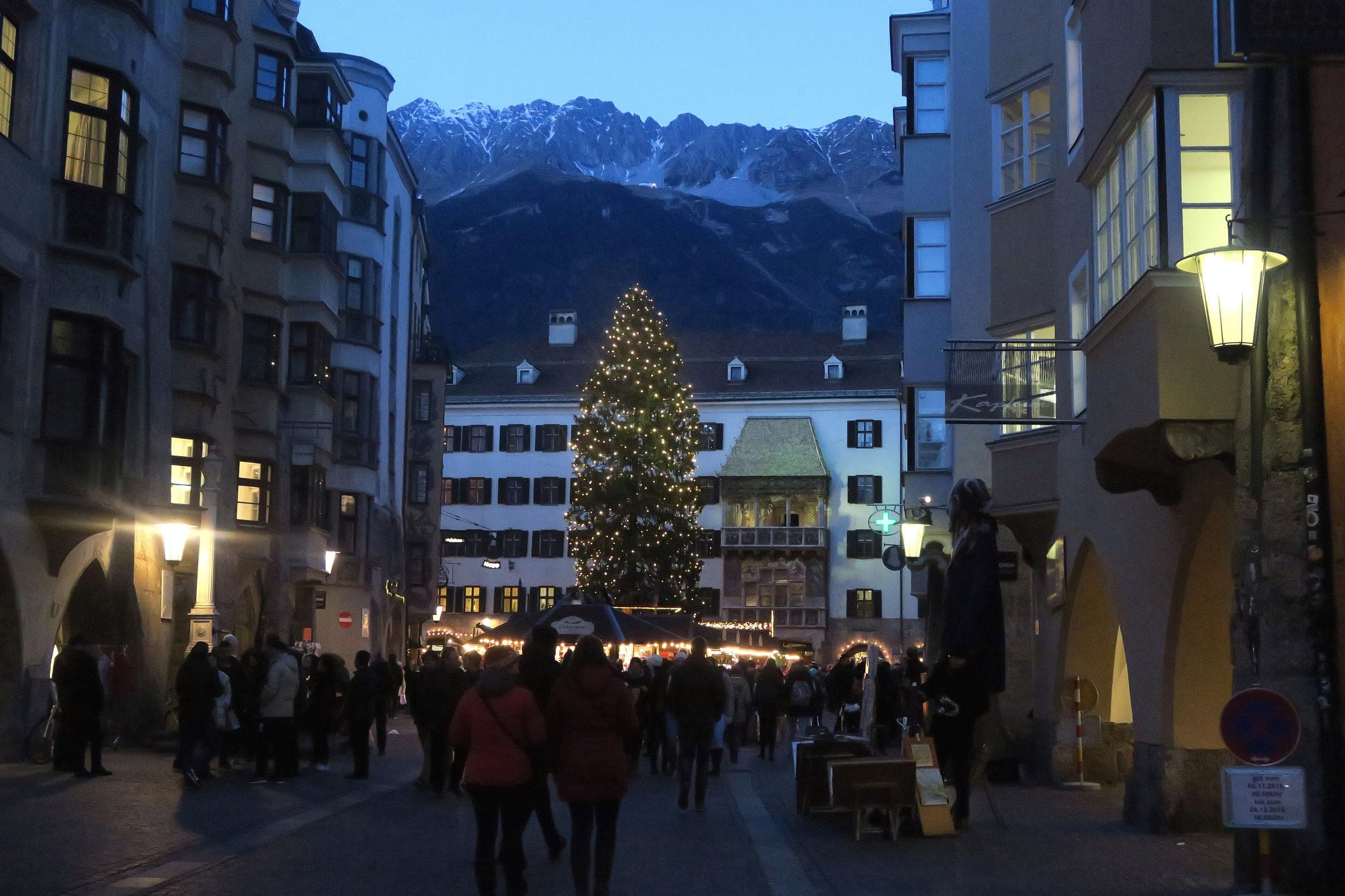 Shoppers walk down Herzog-Friedrich-Straße at dusk toward the lit tree and the Golden Roof below the Nordkette.