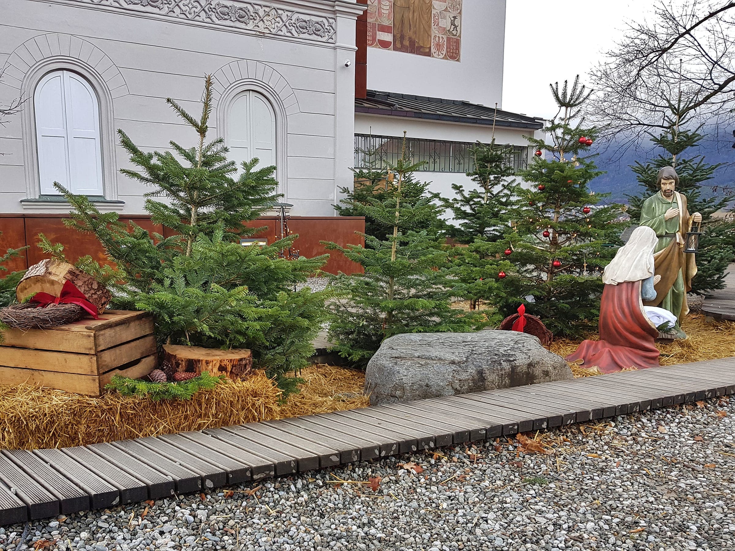 Carved nativity figures stand among young firs and straw at the Bergisel Christmas market in Innsbruck.