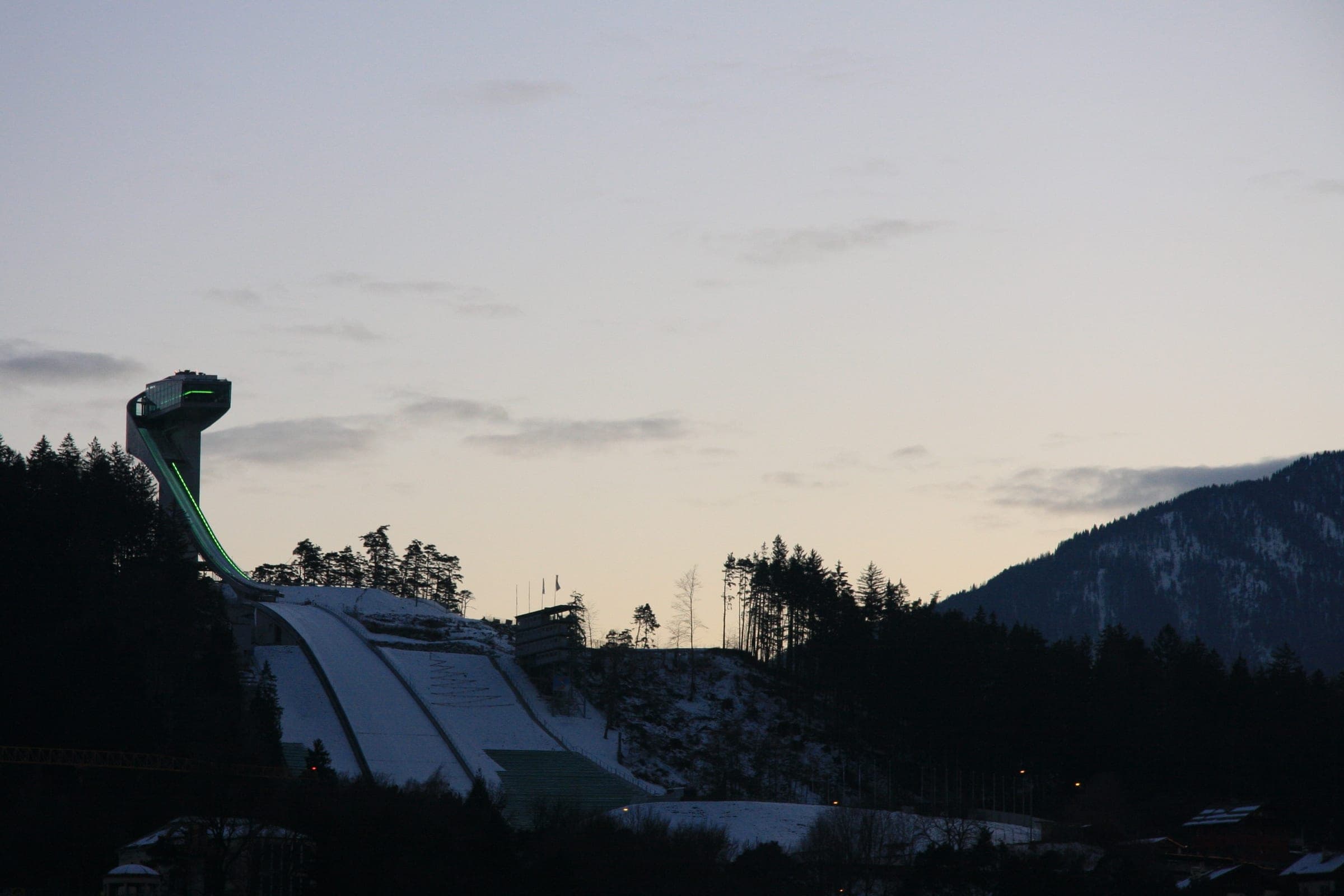 The Bergisel ski jump tower stands dark against a pale January evening sky above Innsbruck.