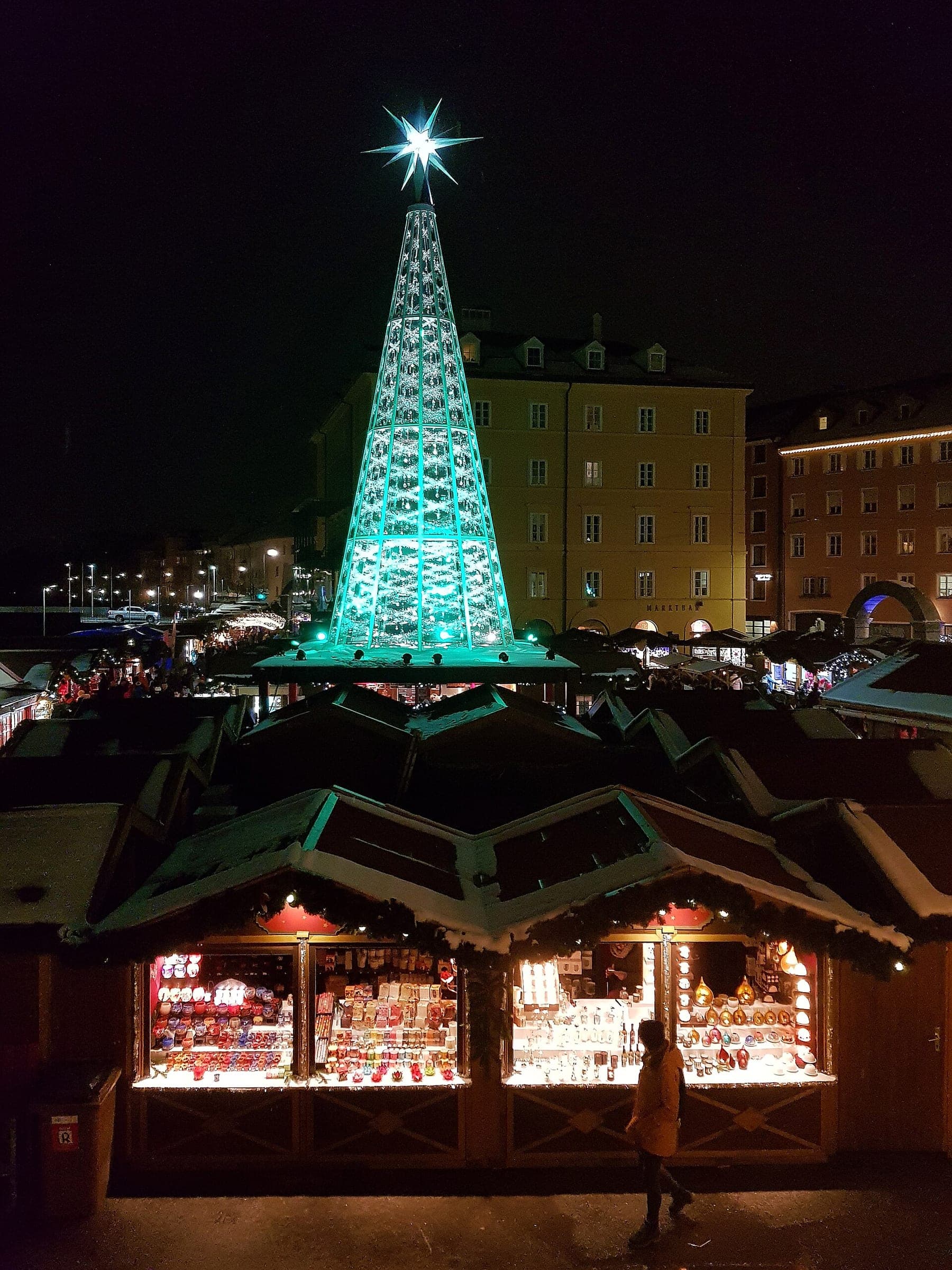 A tall tree of glowing crystals stands above the stall roofs on Innsbruck's Marktplatz at night.