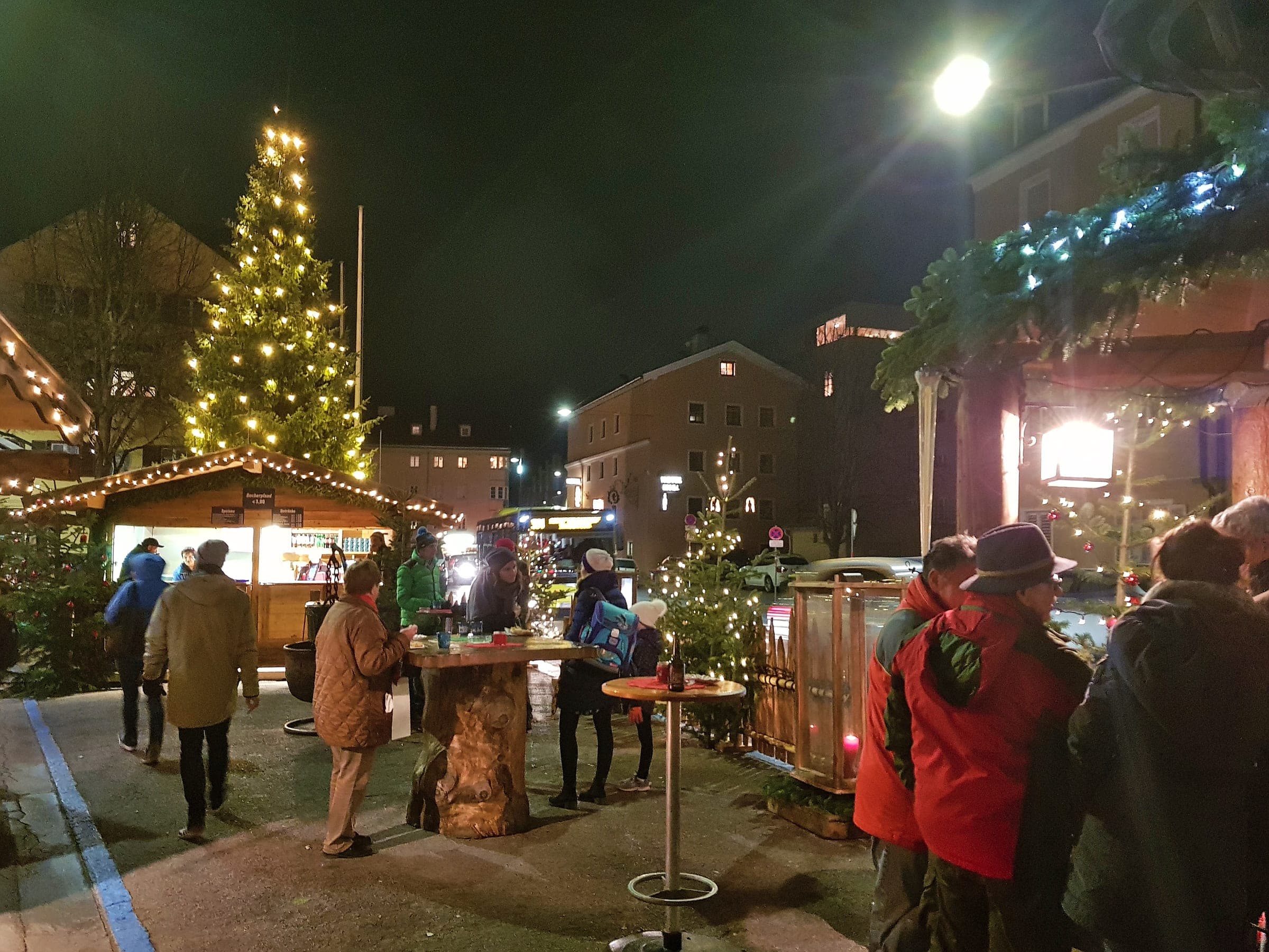 Visitors gather at standing tables under the lit tree at the St. Nikolaus Christmas market in Innsbruck.
