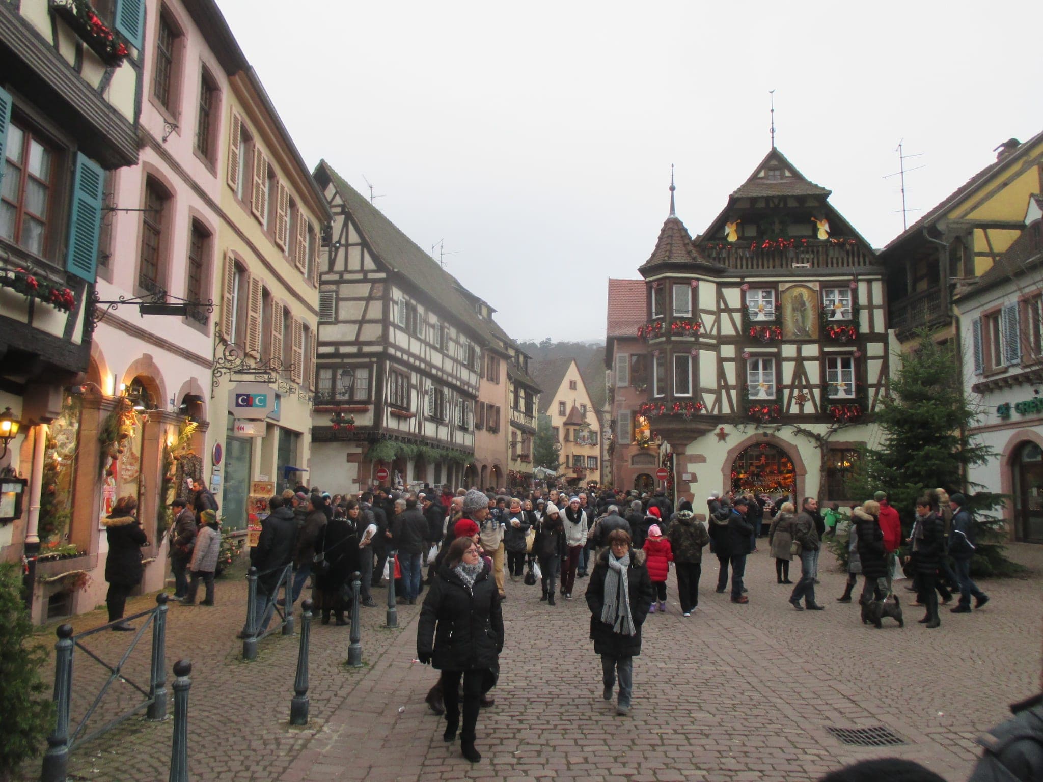 Visitors walk up the Grand'Rue of Kaysersberg toward a turreted half-timbered house during the Christmas market.