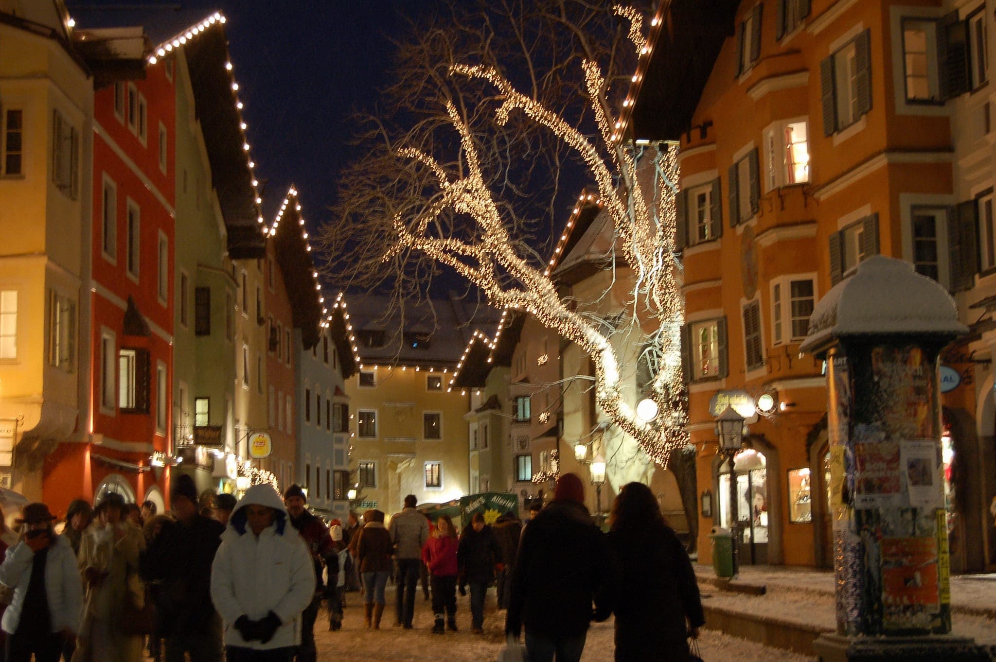 Crowds stroll under lit trees and roofline lights along the Vorderstadt in Kitzbühel during Advent.