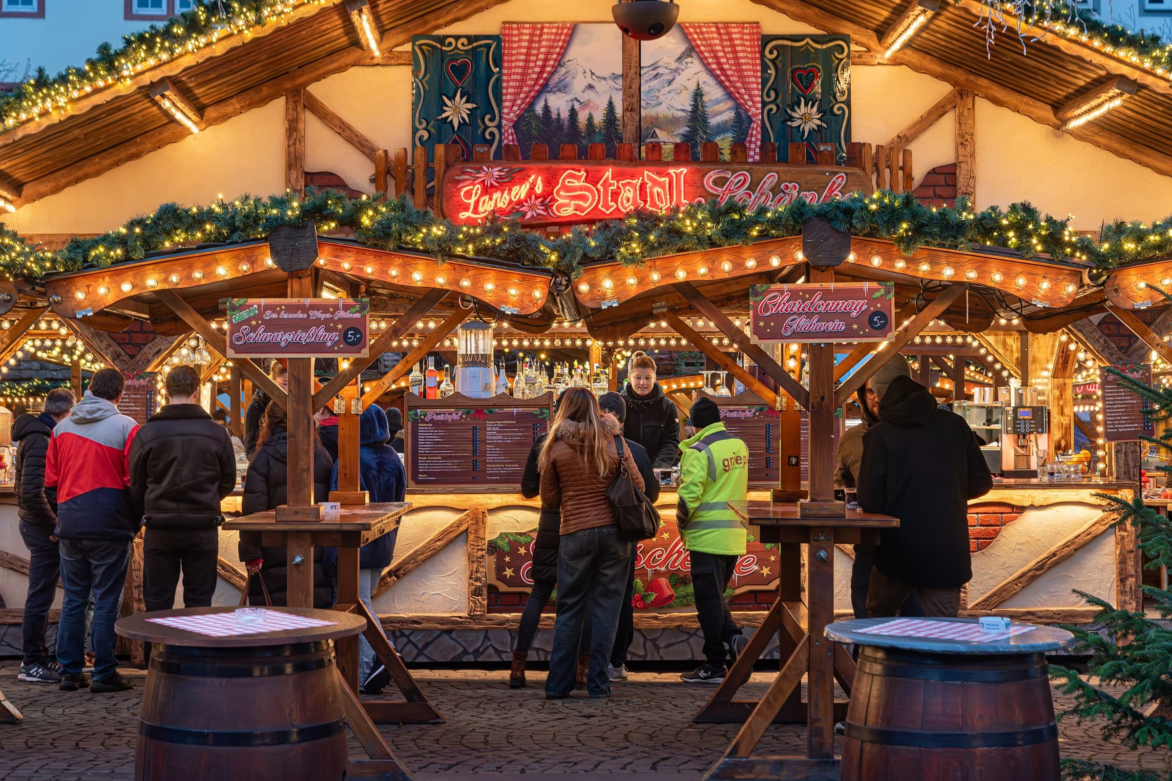 Visitors queue at a garlanded mulled wine hut with barrel tables at the Koblenz Christmas market