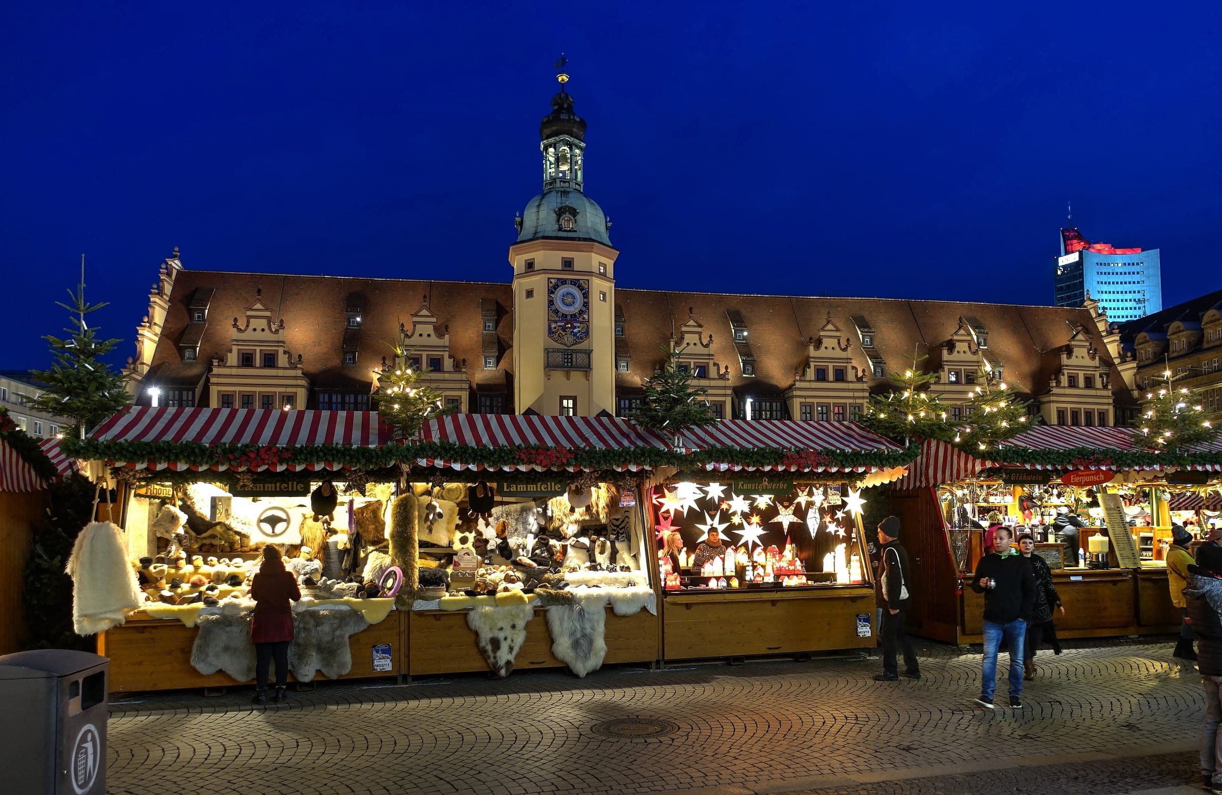 Lit stalls line the front of Leipzig's Renaissance Old Town Hall at the Christmas market at blue hour.