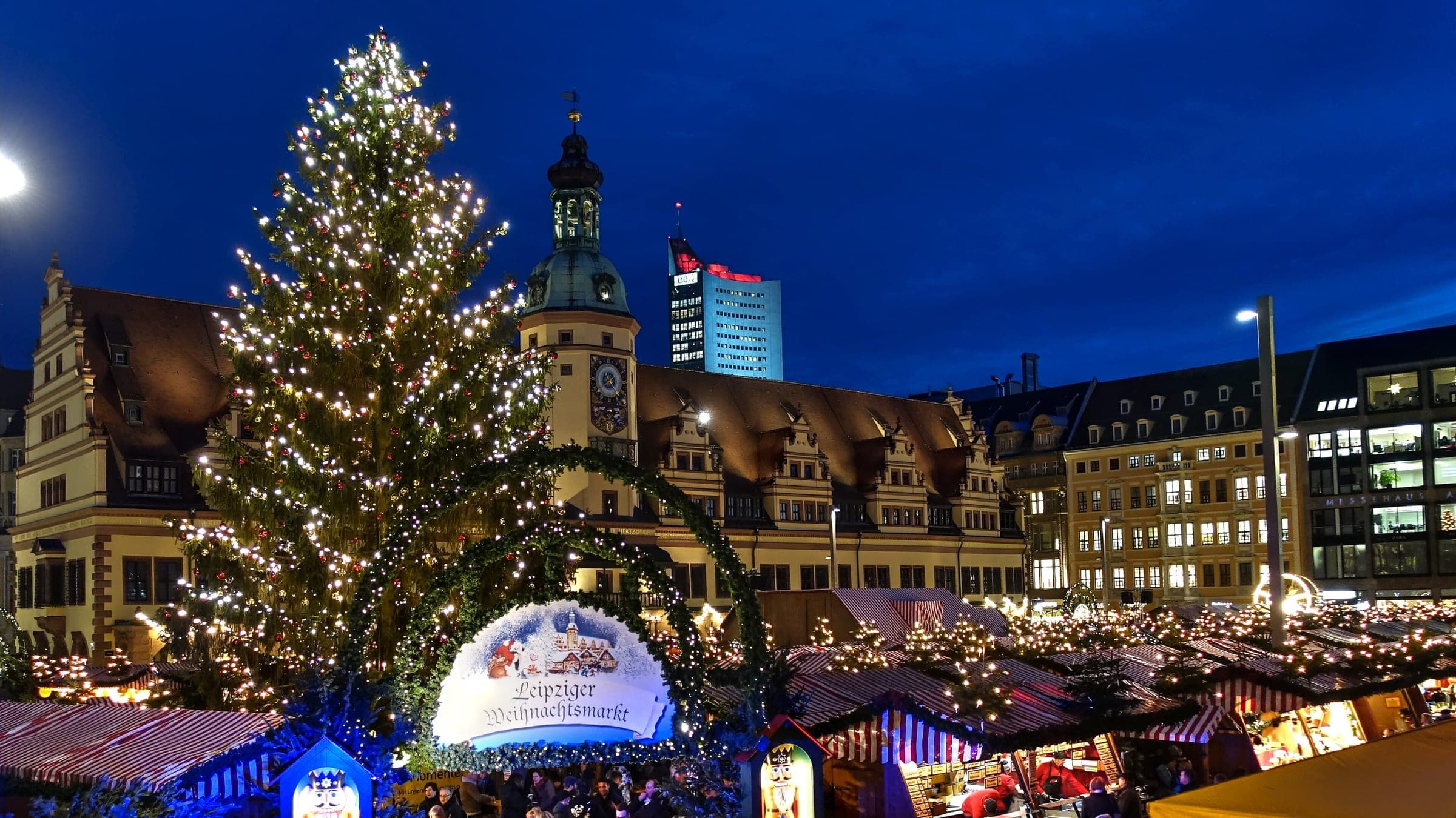 The Christmas tree and lit stall roofs fill Leipzig's Markt below the Old Town Hall tower at dusk.