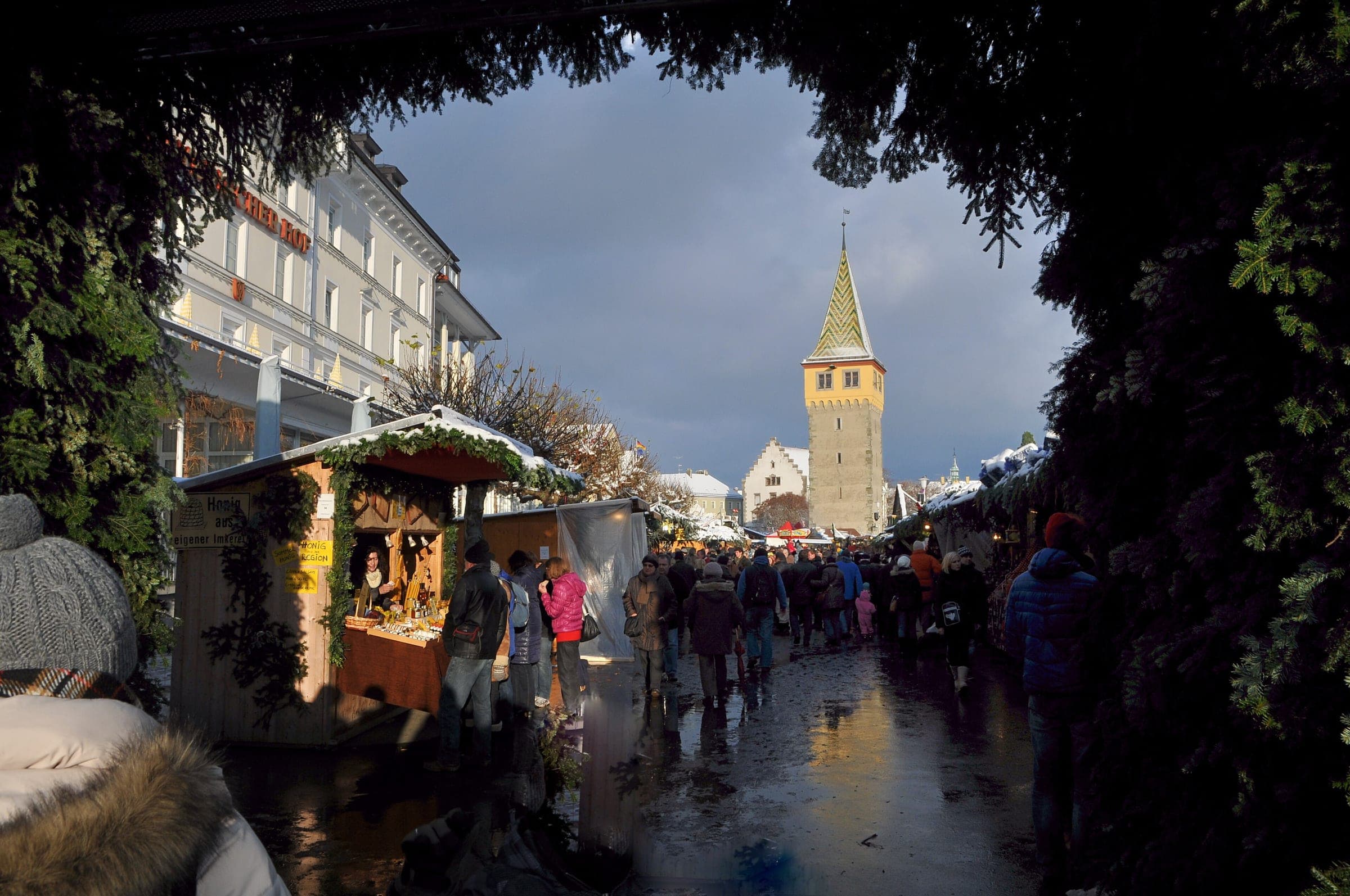 A garland arch frames the stalls of the Lindau Hafenweihnacht and the Mangturm after a rain shower.
