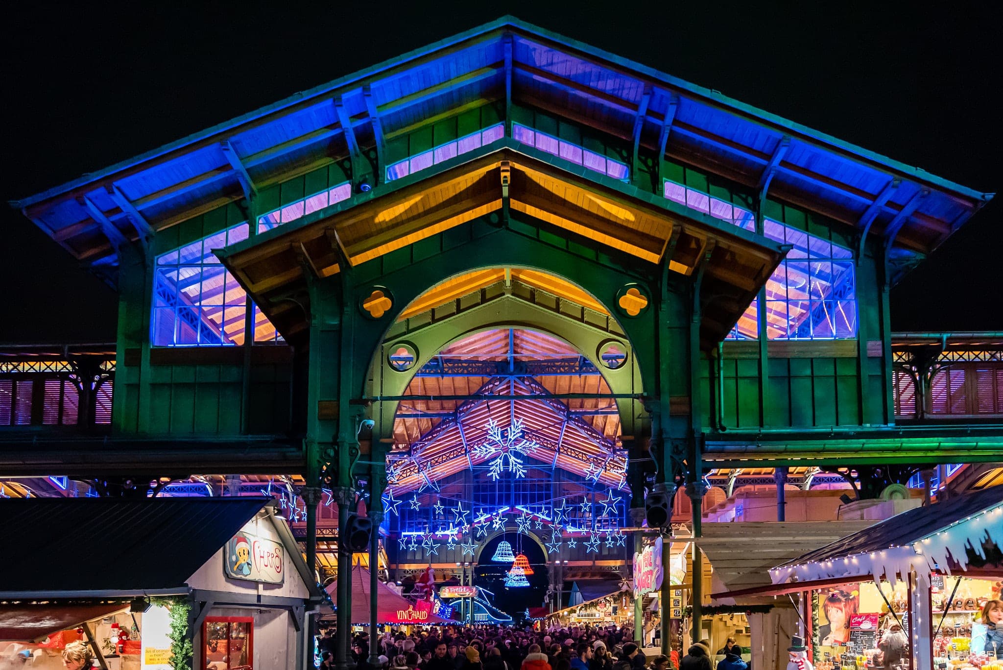 The old market hall on Place du Marché in Montreux glows in blue and gold above the Christmas stalls at night