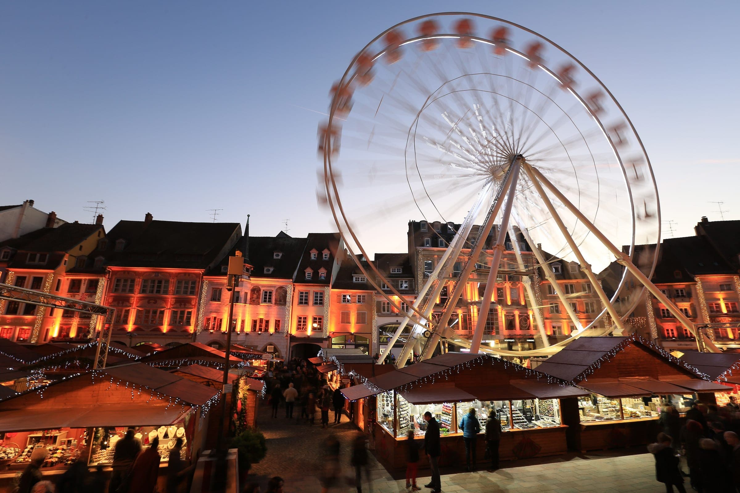 The Ferris wheel turns above the chalet roofs of the Mulhouse Christmas market as dusk lights the old facades.