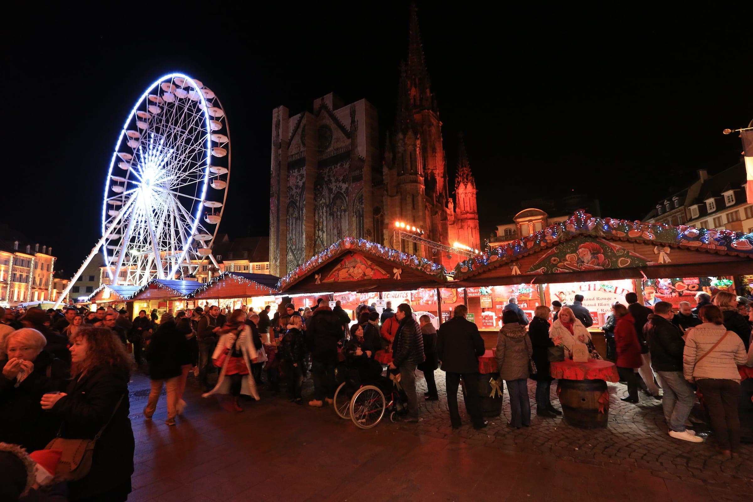 Crowds browse the stalls on Place de la Réunion in Mulhouse below the Ferris wheel and the Temple Saint-Étienne.