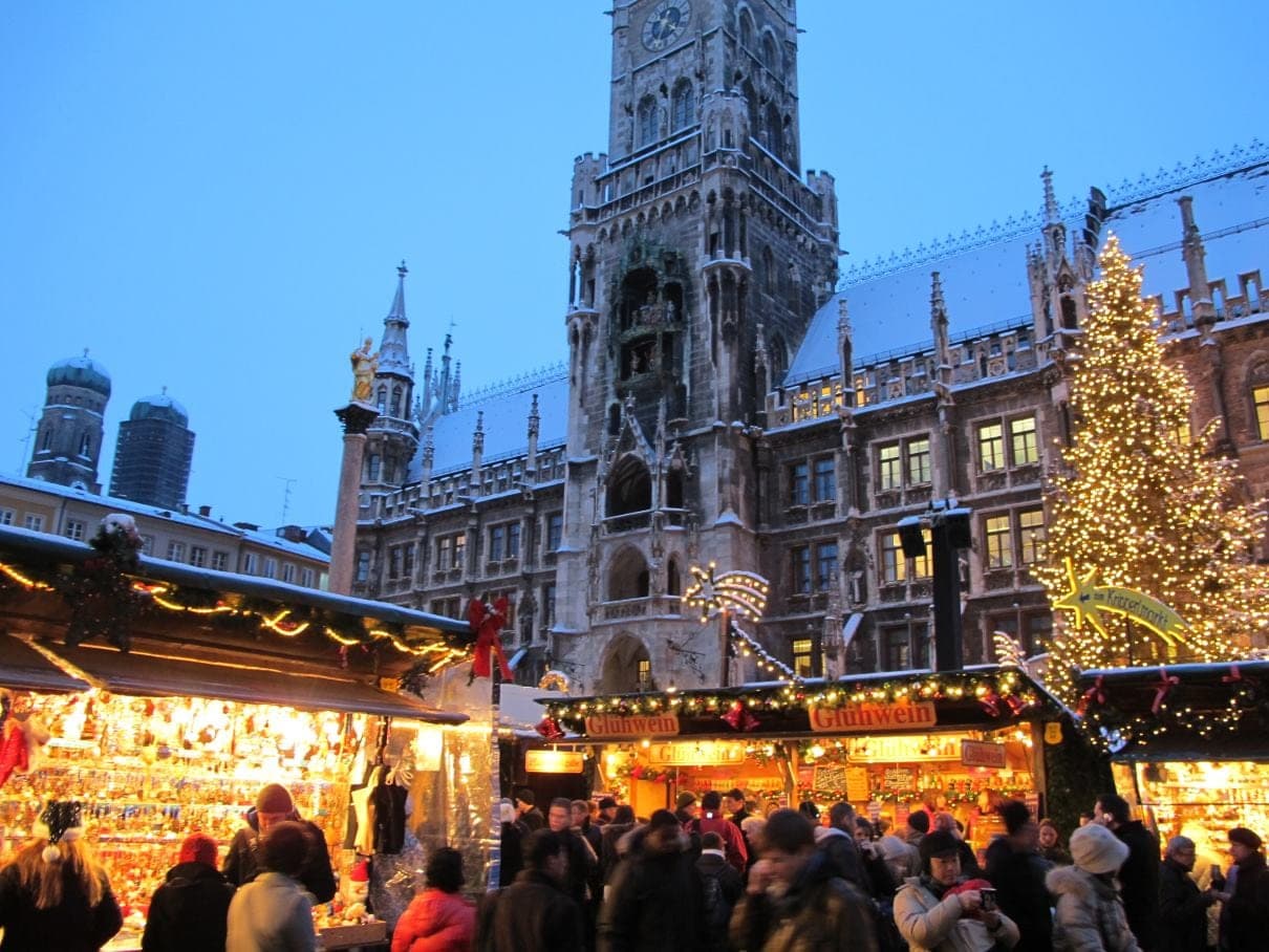 Crowds fill the Marienplatz Christkindlmarkt at blue hour under the Neues Rathaus tower and the Christmas tree.