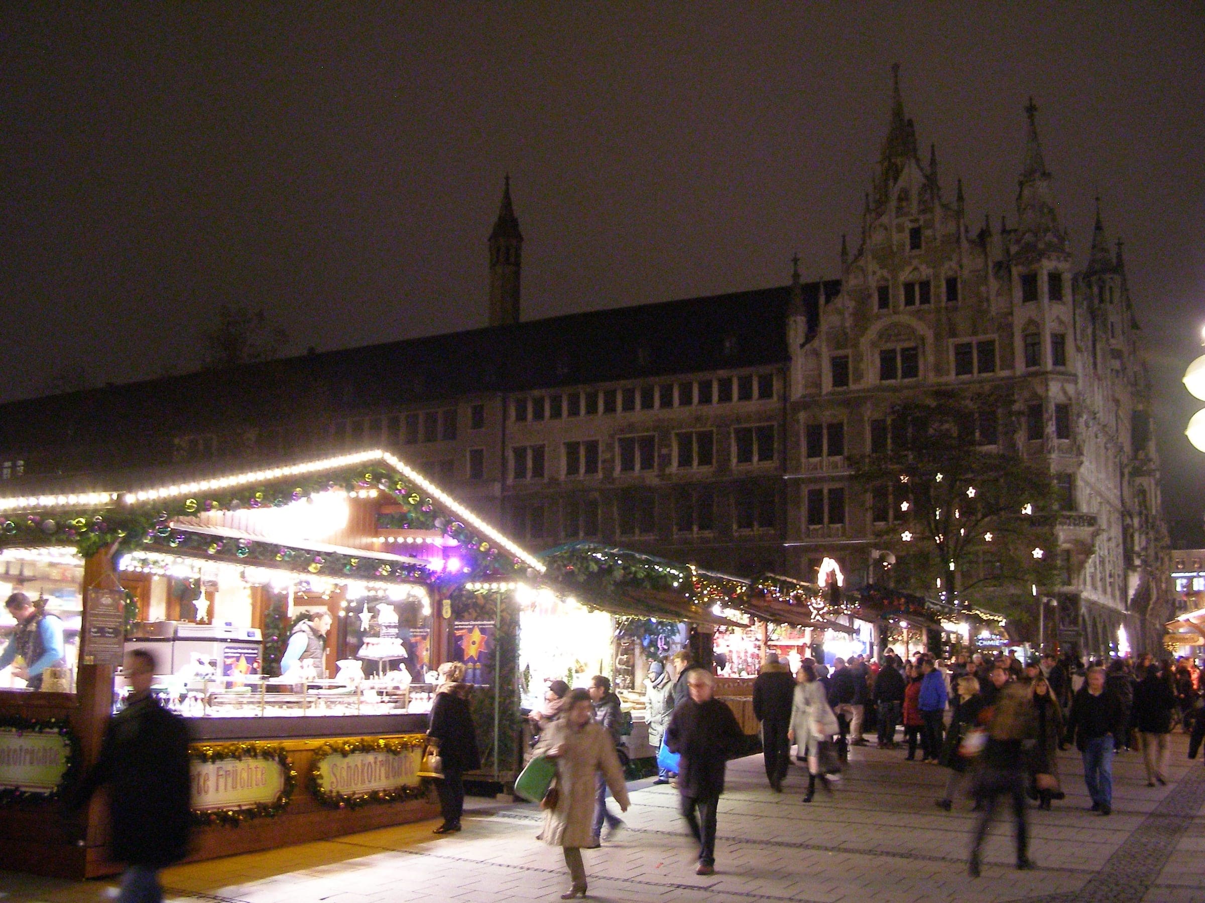 Lit stalls of the Munich Christkindlmarkt line Weinstraße at night beside the Neues Rathaus.