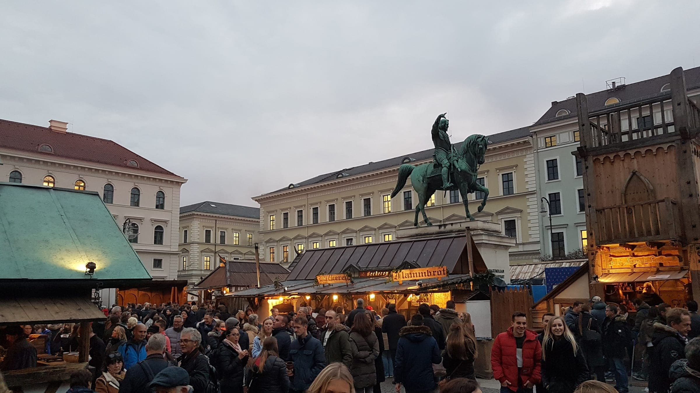 Timber stalls glow at dusk as visitors pack the medieval Christmas market on Munich's Wittelsbacherplatz.