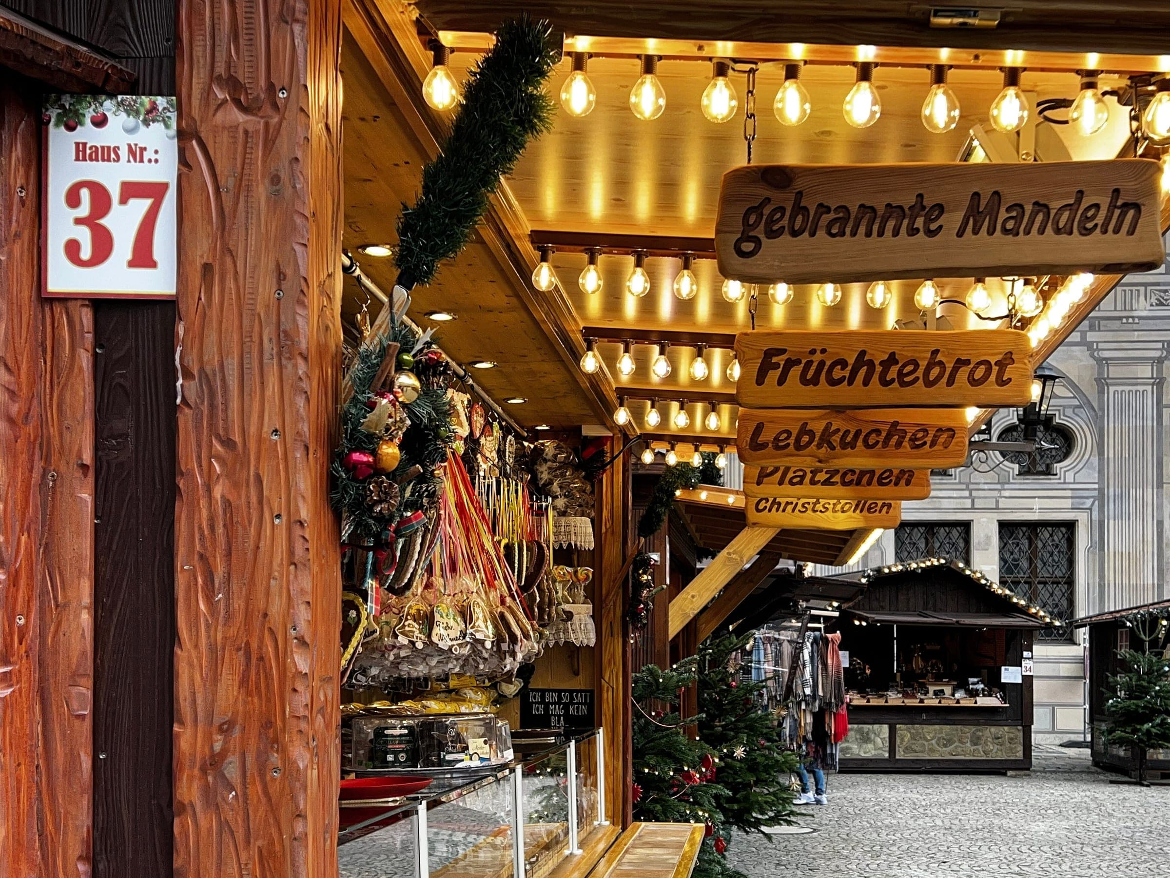Wooden huts with warm lights and carved signs line the Kaiserhof of the Munich Residenz at the Christmas village.