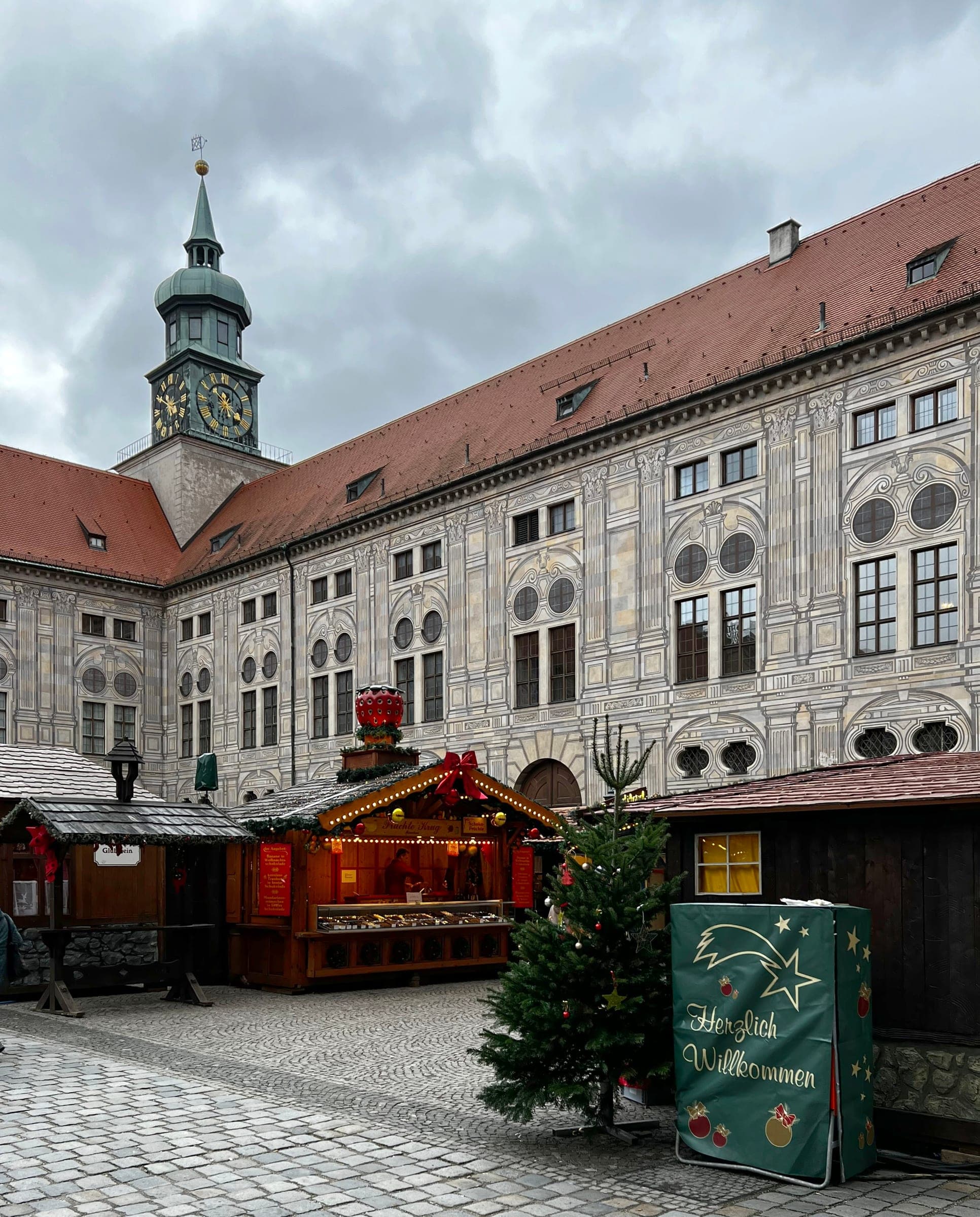 A lit hut and a small Christmas tree stand in the Kaiserhof courtyard under the clock tower of the Munich Residenz.