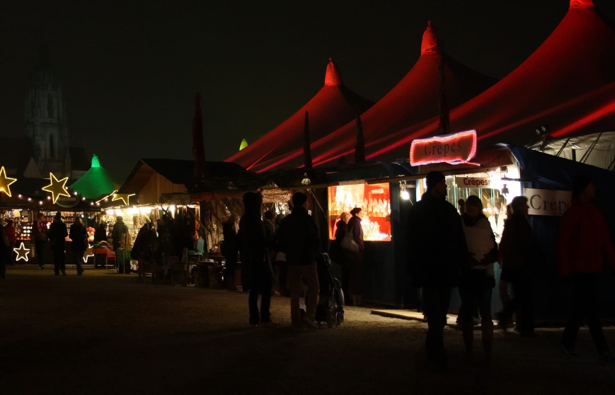 Visitors walk between lit stalls under the red tent roofs of the Tollwood Winter Festival in Munich.