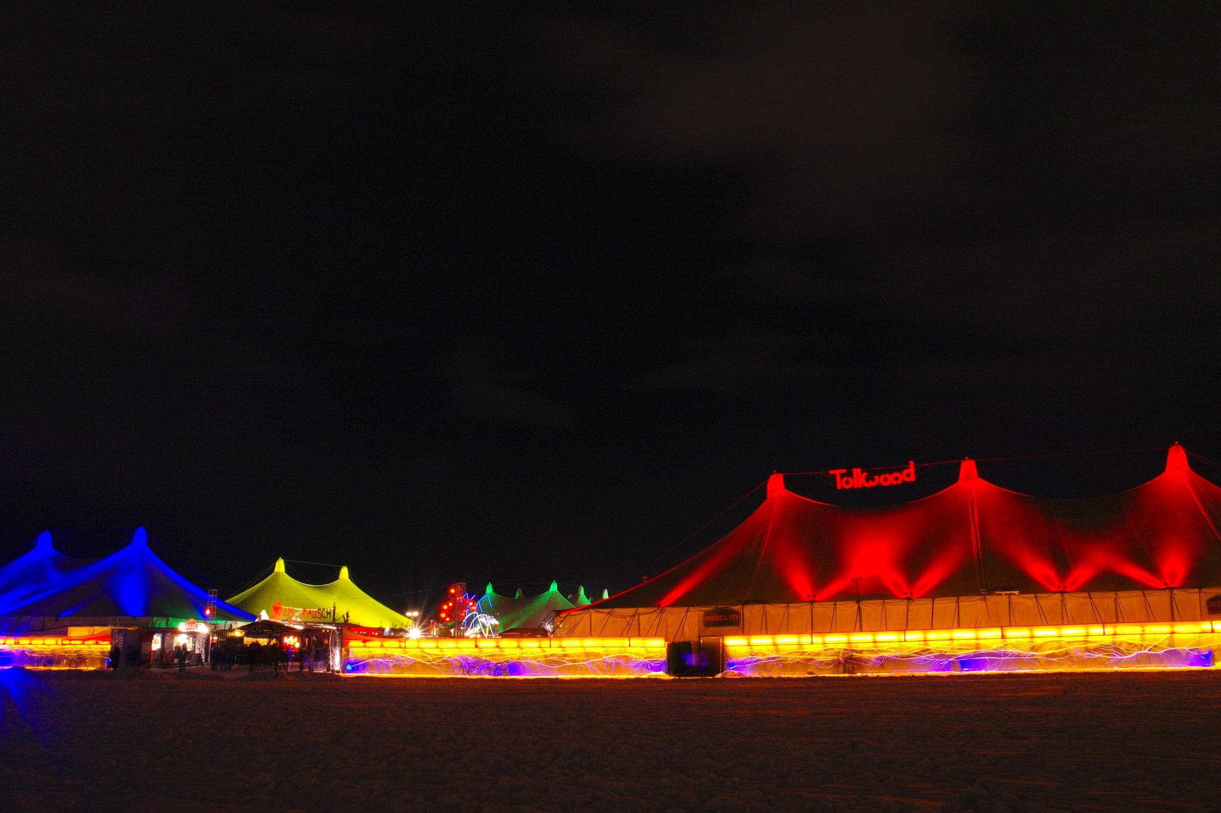 The big tents of the Tollwood Winter Festival glow red, blue and green across Munich's Theresienwiese at night.