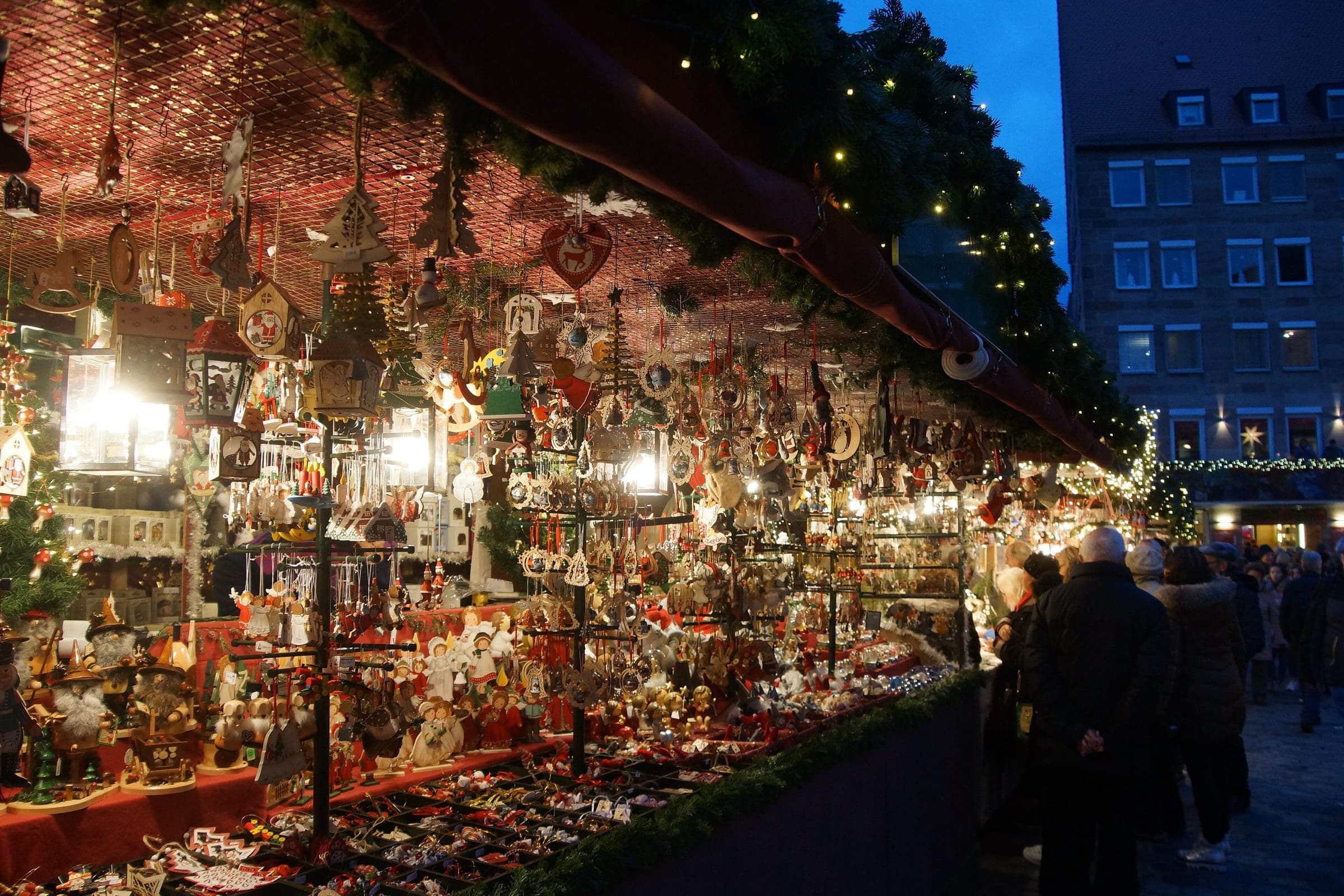 Glass ornaments and lanterns hang in a lit stall at the Nuremberg Christkindlesmarkt as the sky turns dark blue
