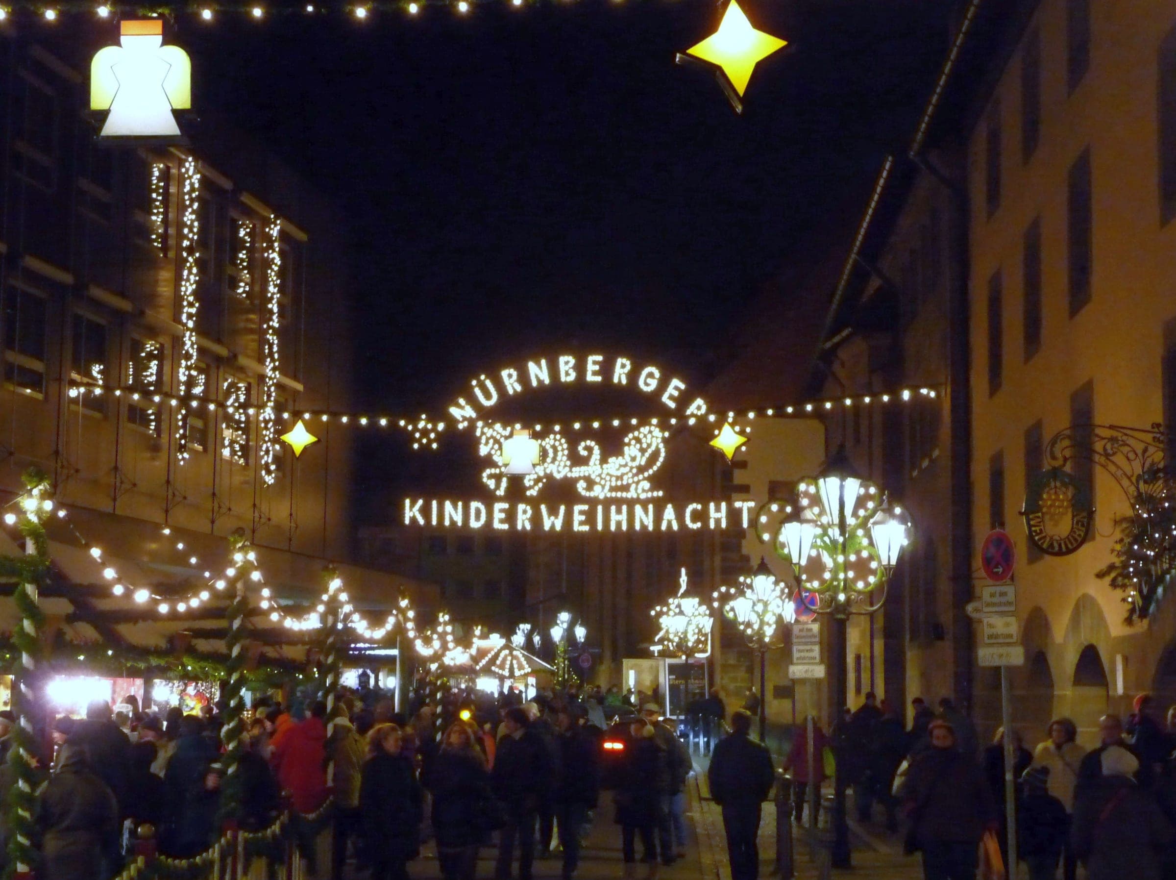 A lit arch spells out Nürnberger Kinderweihnacht above an evening crowd walking between the stalls