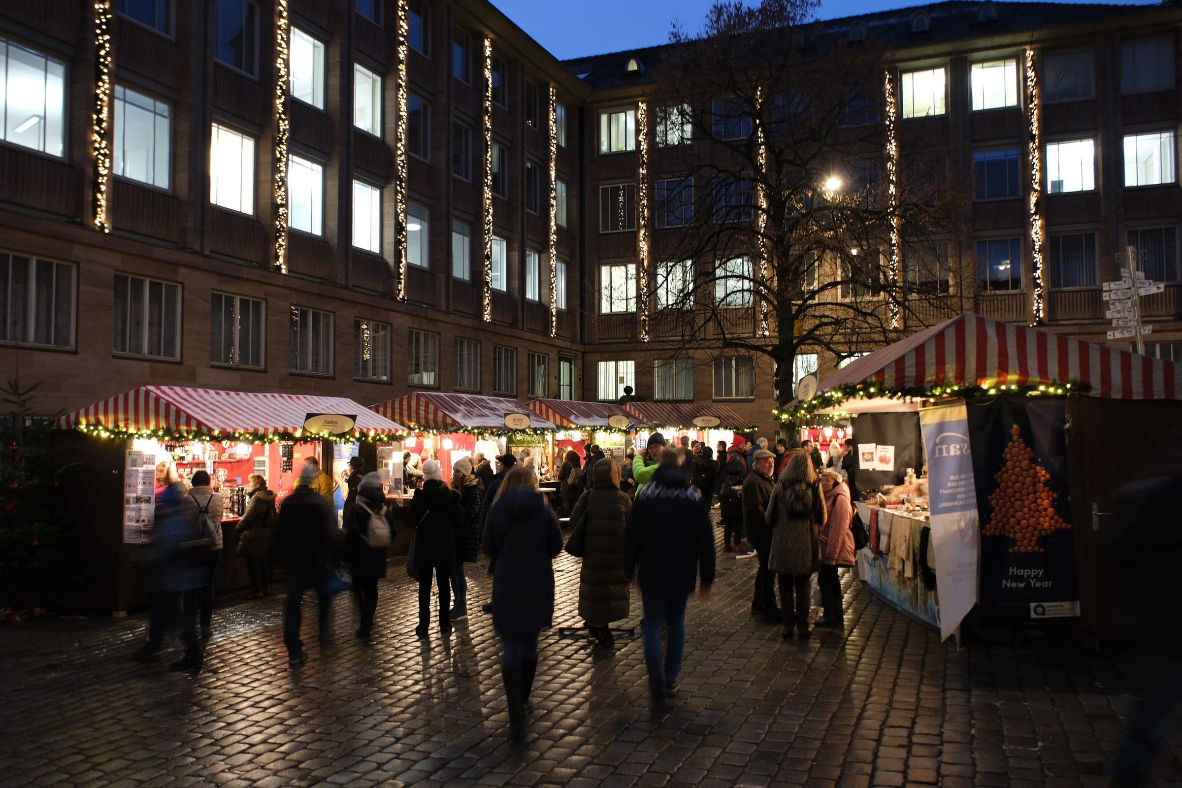 Shoppers walk past the lit stalls of Nuremberg's Markt der Partnerstädte below a building hung with lights