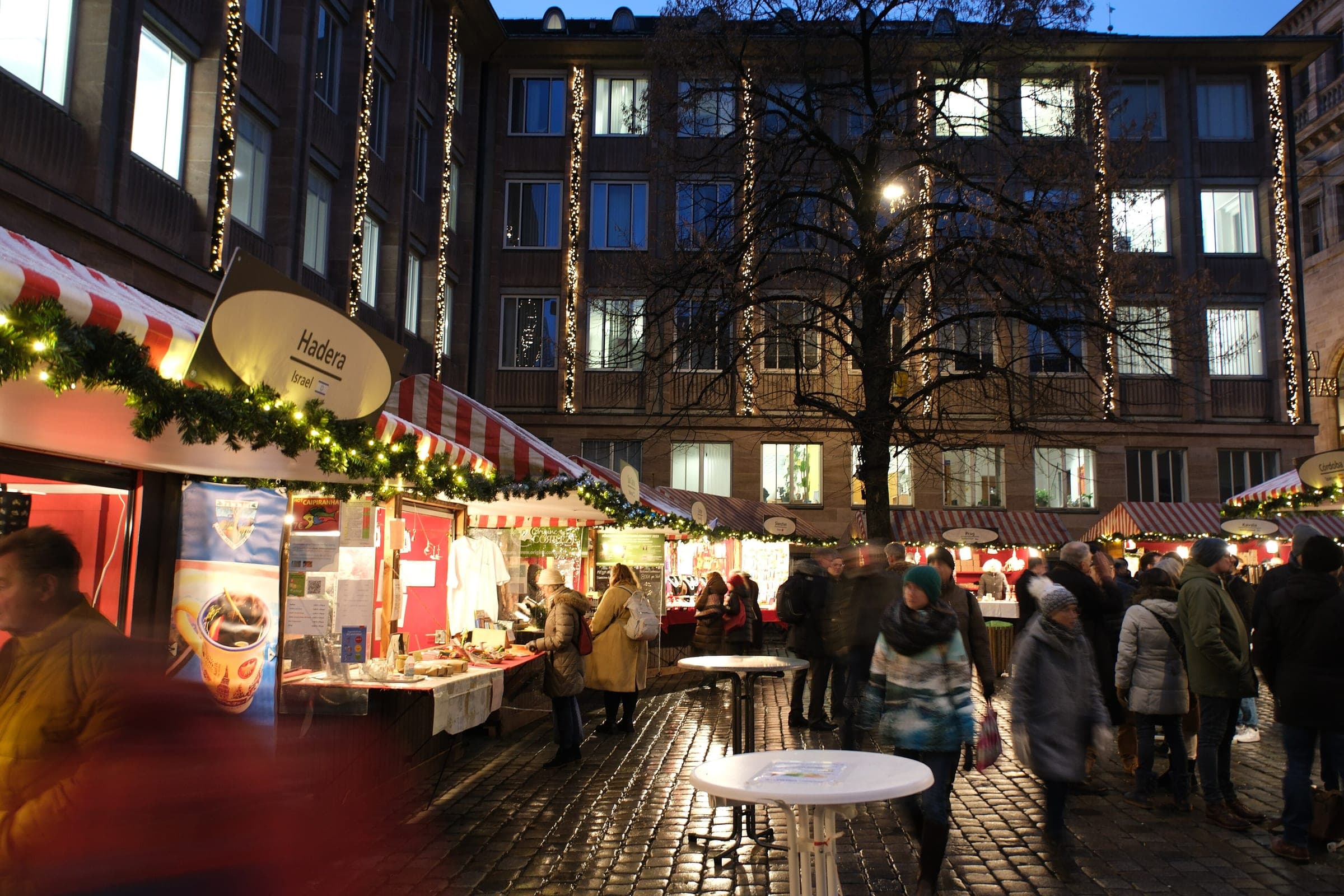 Standing tables and garlanded stalls fill the square at Nuremberg's Markt der Partnerstädte on a December evening