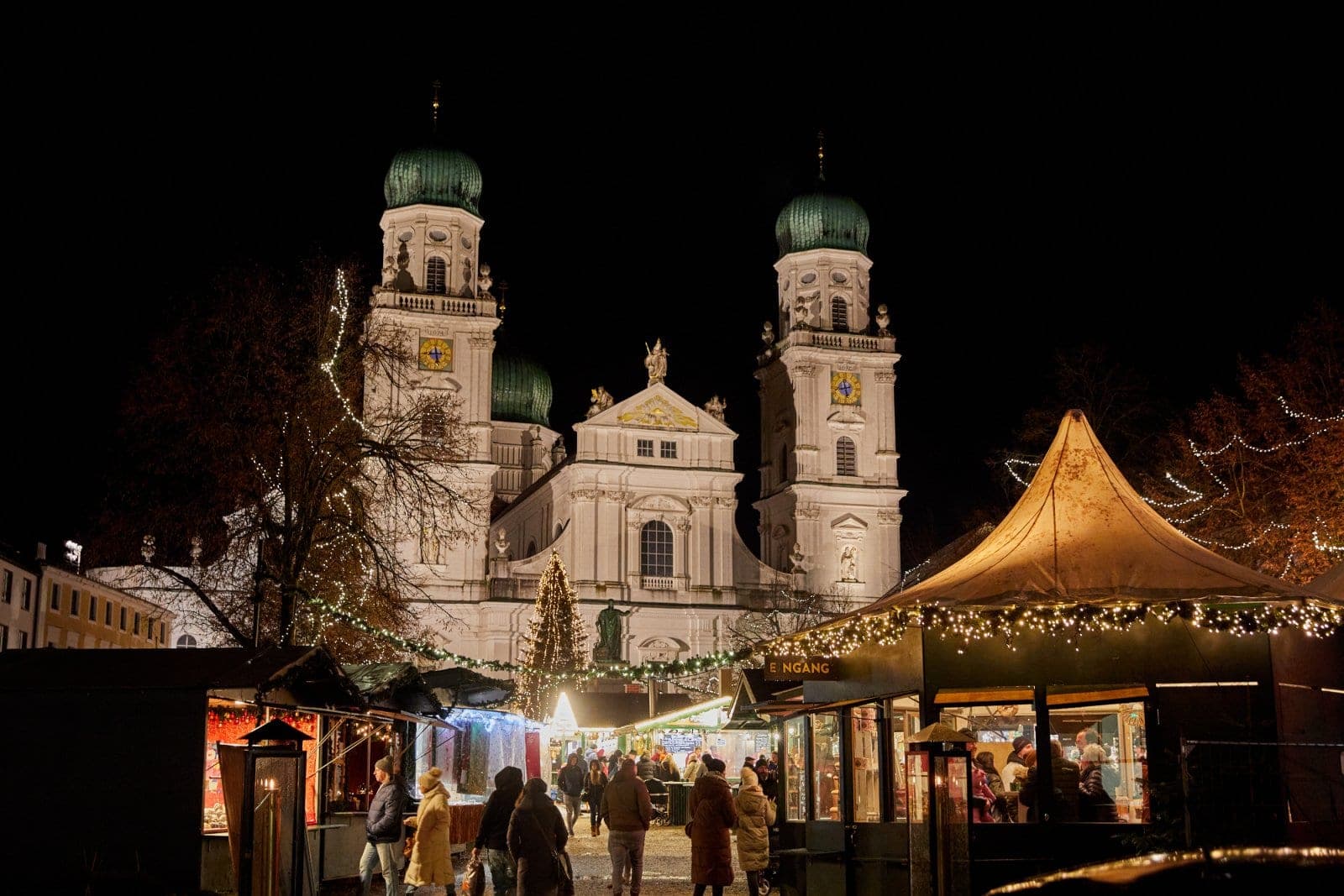 Lit stalls of the Passau Christkindlmarkt stand on Domplatz below the floodlit towers of St. Stephen's Cathedral.