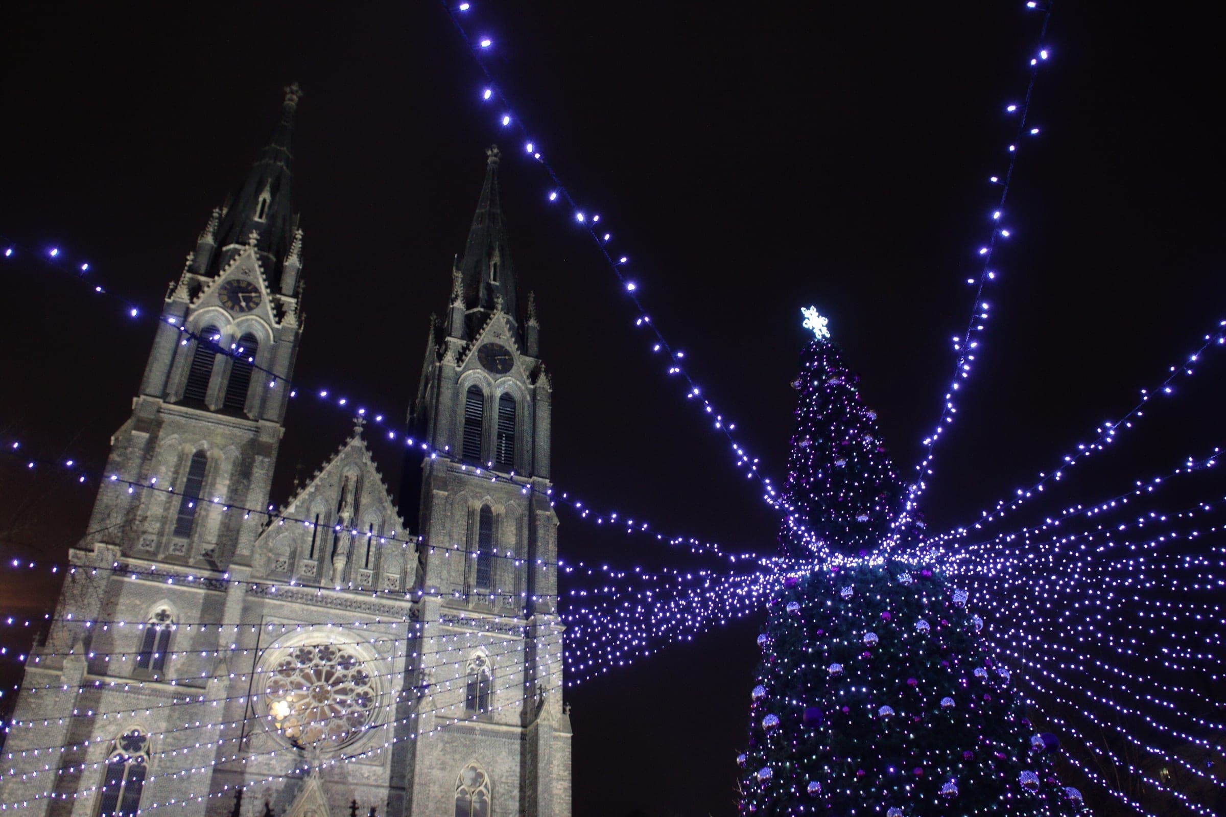Blue lights stream from the Christmas tree over the náměstí Míru market toward the twin spires of St Ludmila.