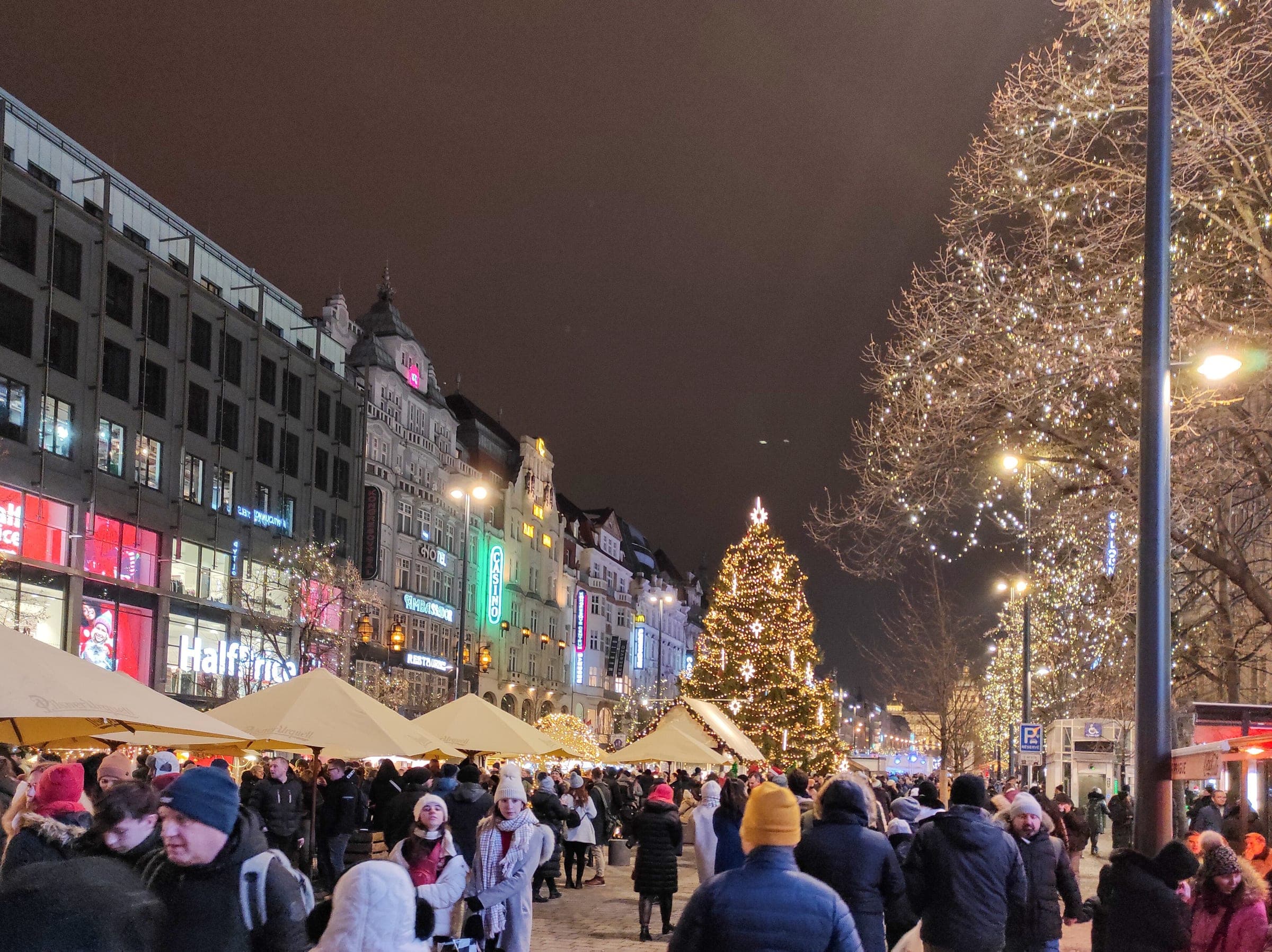 Market stalls and a lit Christmas tree fill the lower end of Wenceslas Square in Prague on a December evening.
