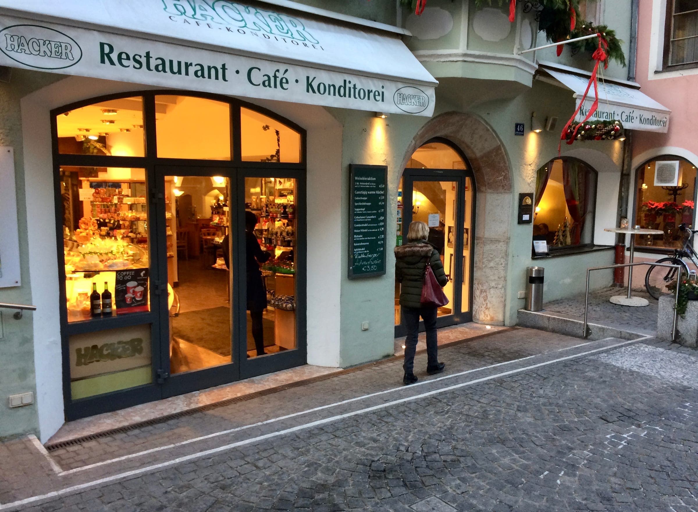 A red-ribboned garland hangs over the lit windows of a café and pastry shop in Rattenberg in December.