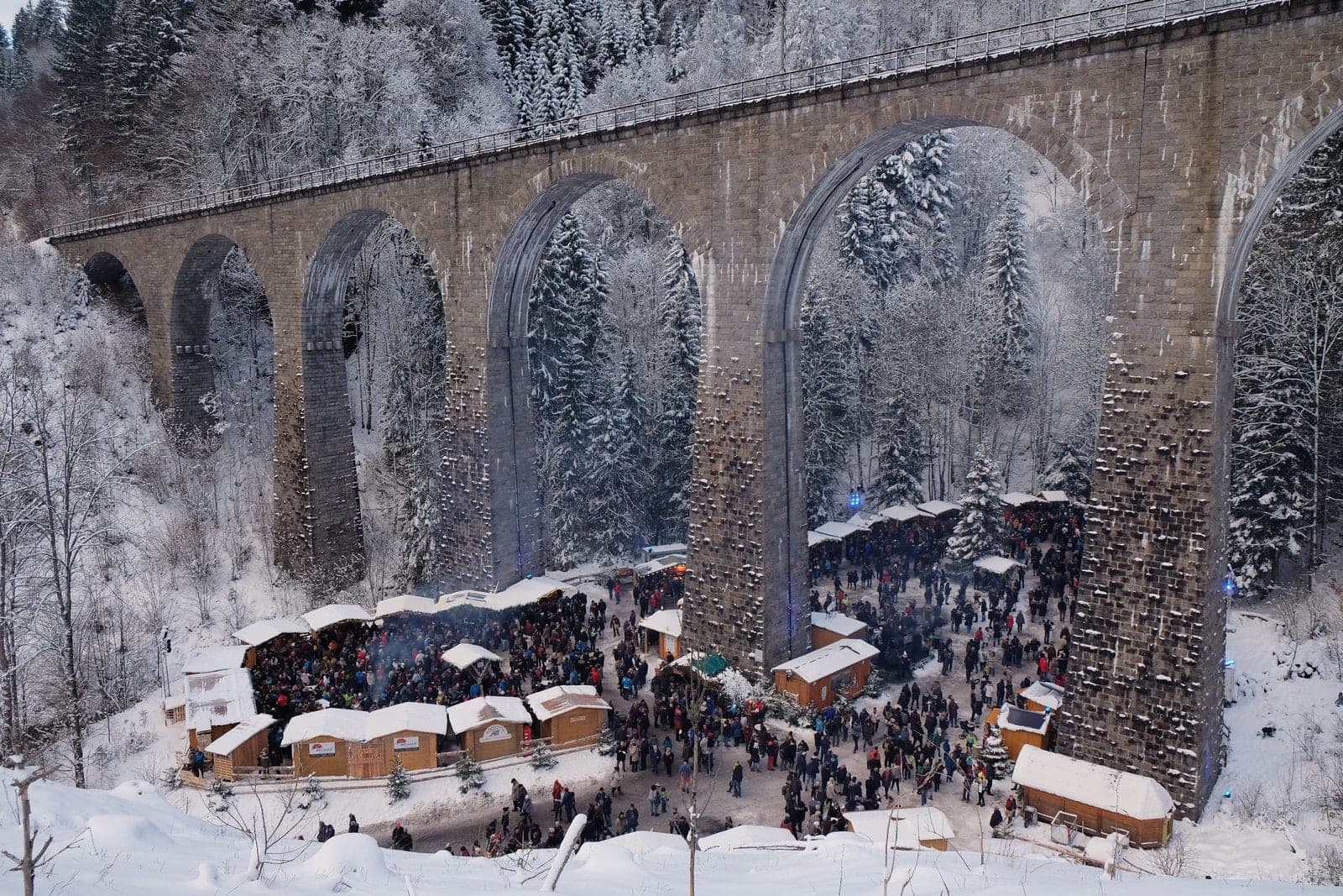 Snowy stall roofs and crowds fill the floor of the Ravenna Gorge below the stone arches of the viaduct.