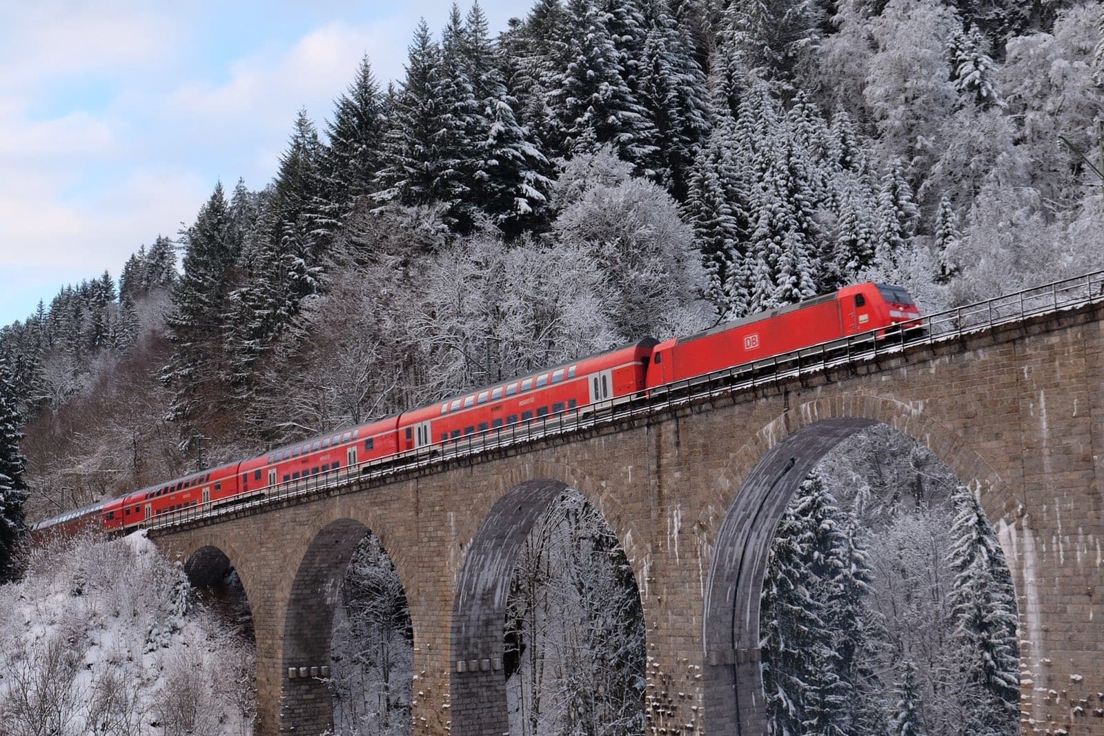 A red Höllentalbahn train crosses the Ravenna viaduct between snow-laden firs in the Black Forest.