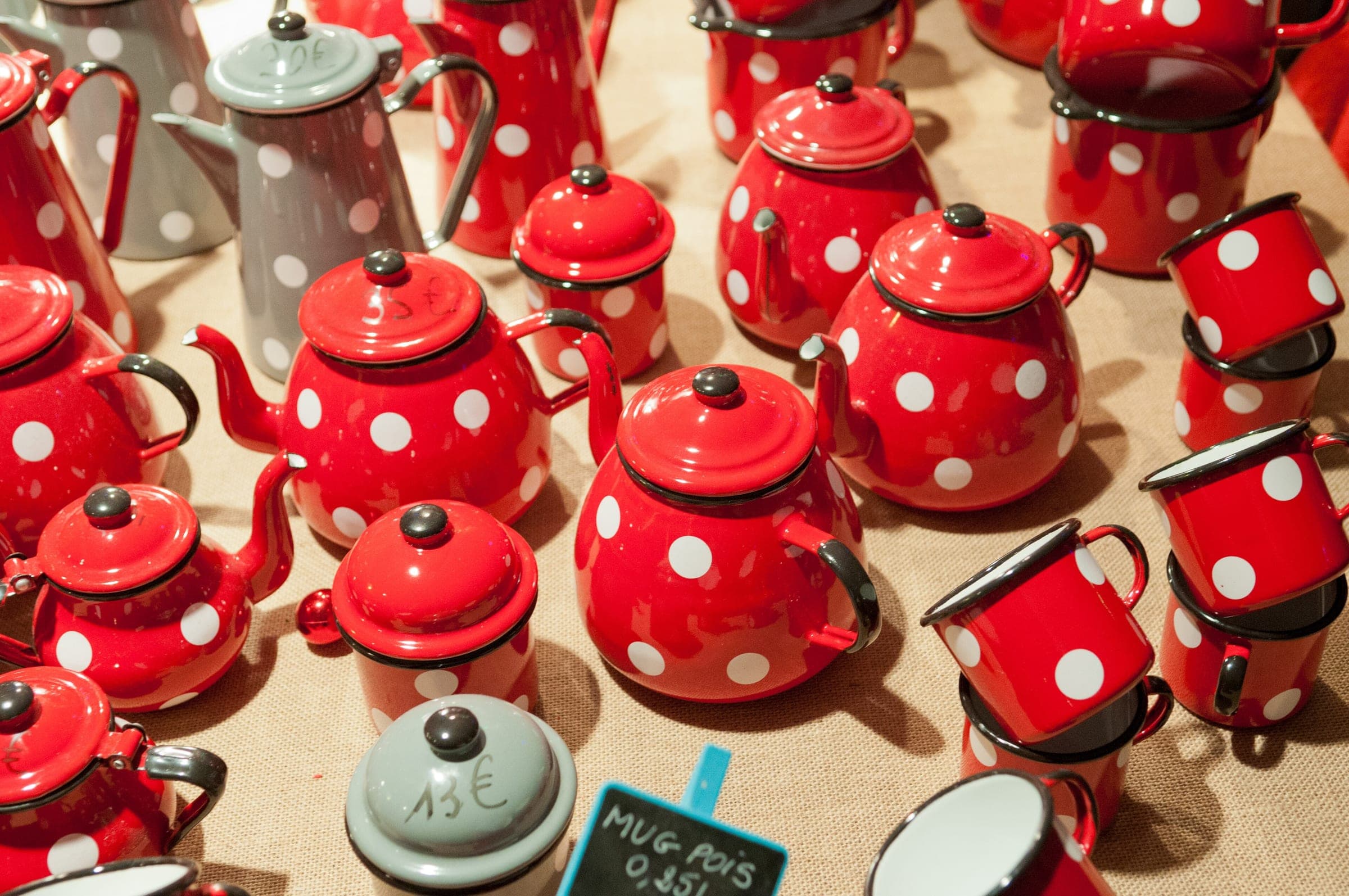 Red enamel teapots and mugs with white polka dots crowd a market table in Riquewihr.
