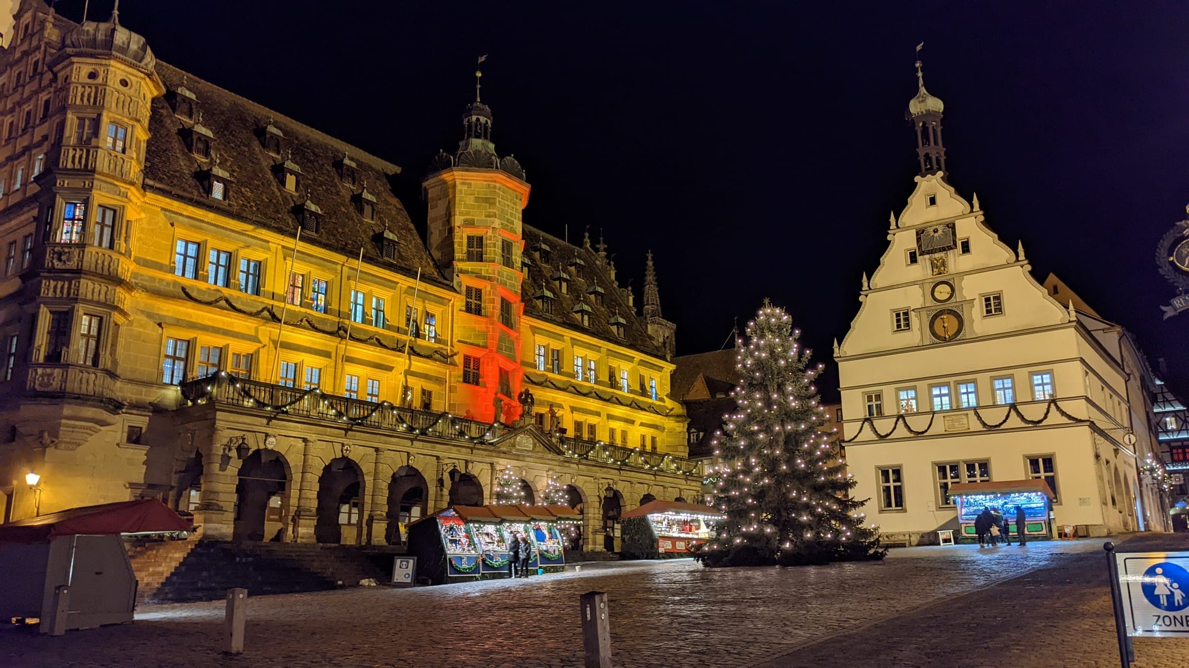 A lit Christmas tree and the floodlit Rathaus face each other across Rothenburg's Marktplatz at night