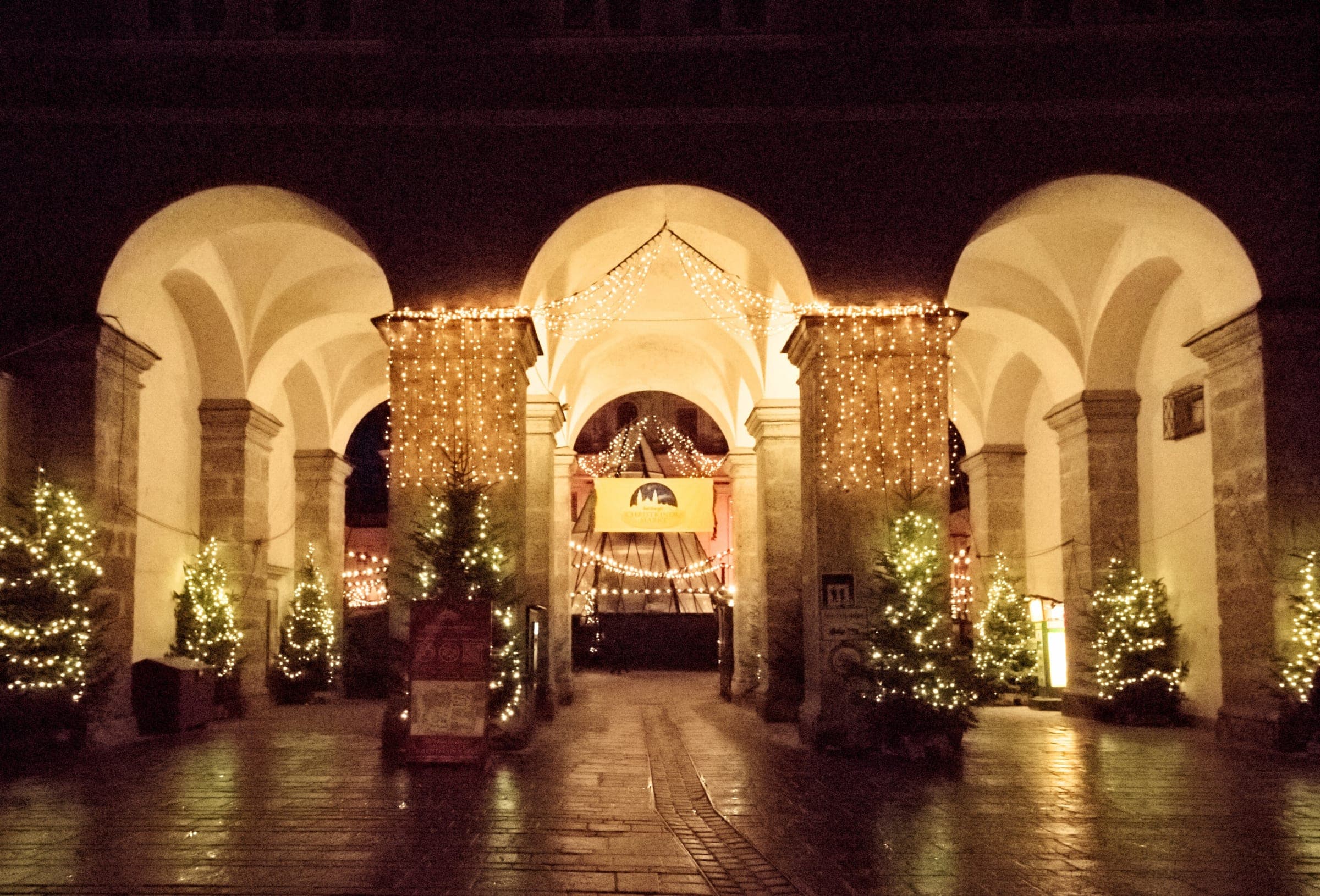 Lit Christmas trees stand under the Dombögen arches at the entrance to Salzburg's Domplatz