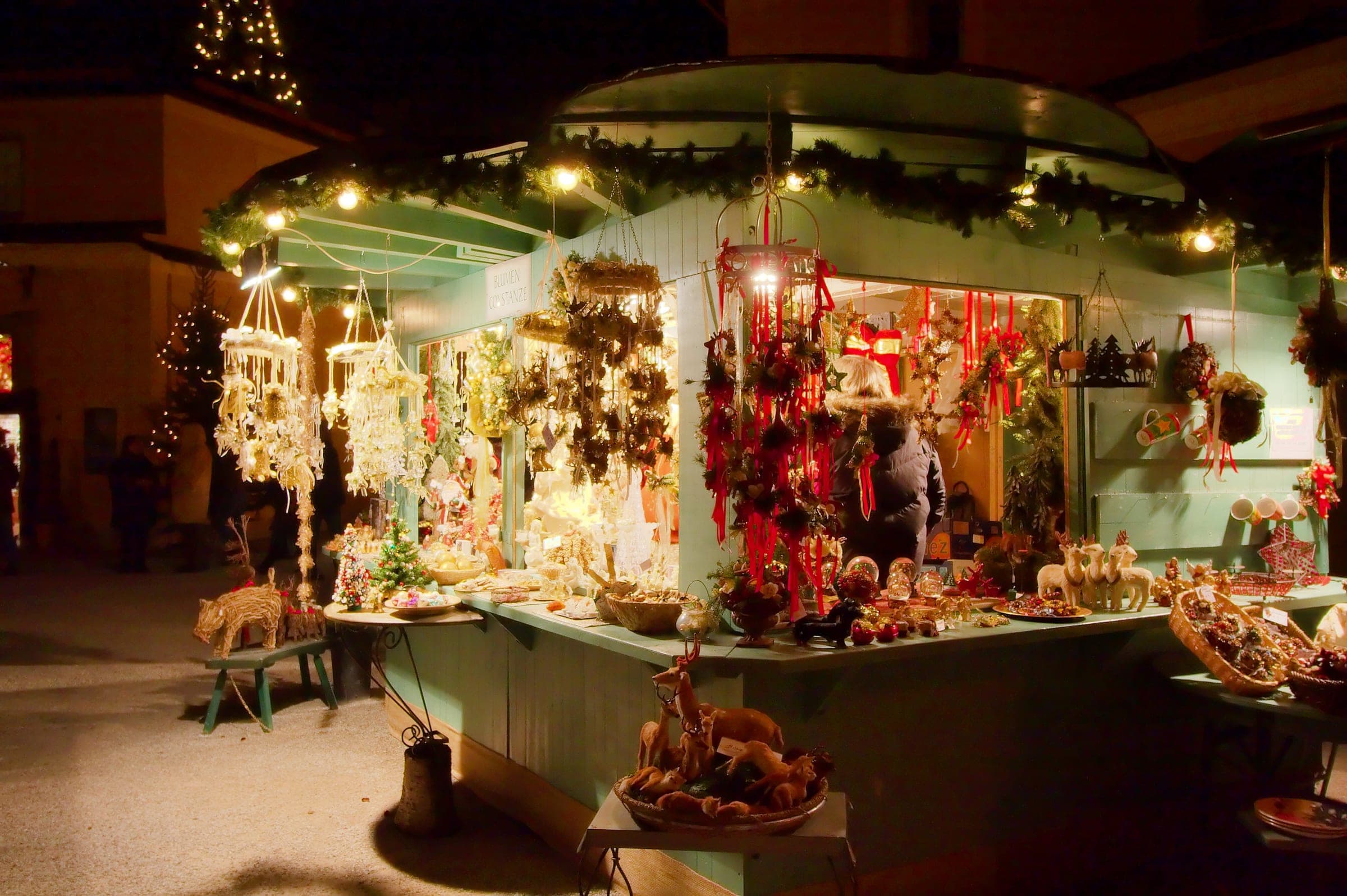 Straw stars and red ornaments hang in a lit stall at the Hellbrunn Advent market after dark