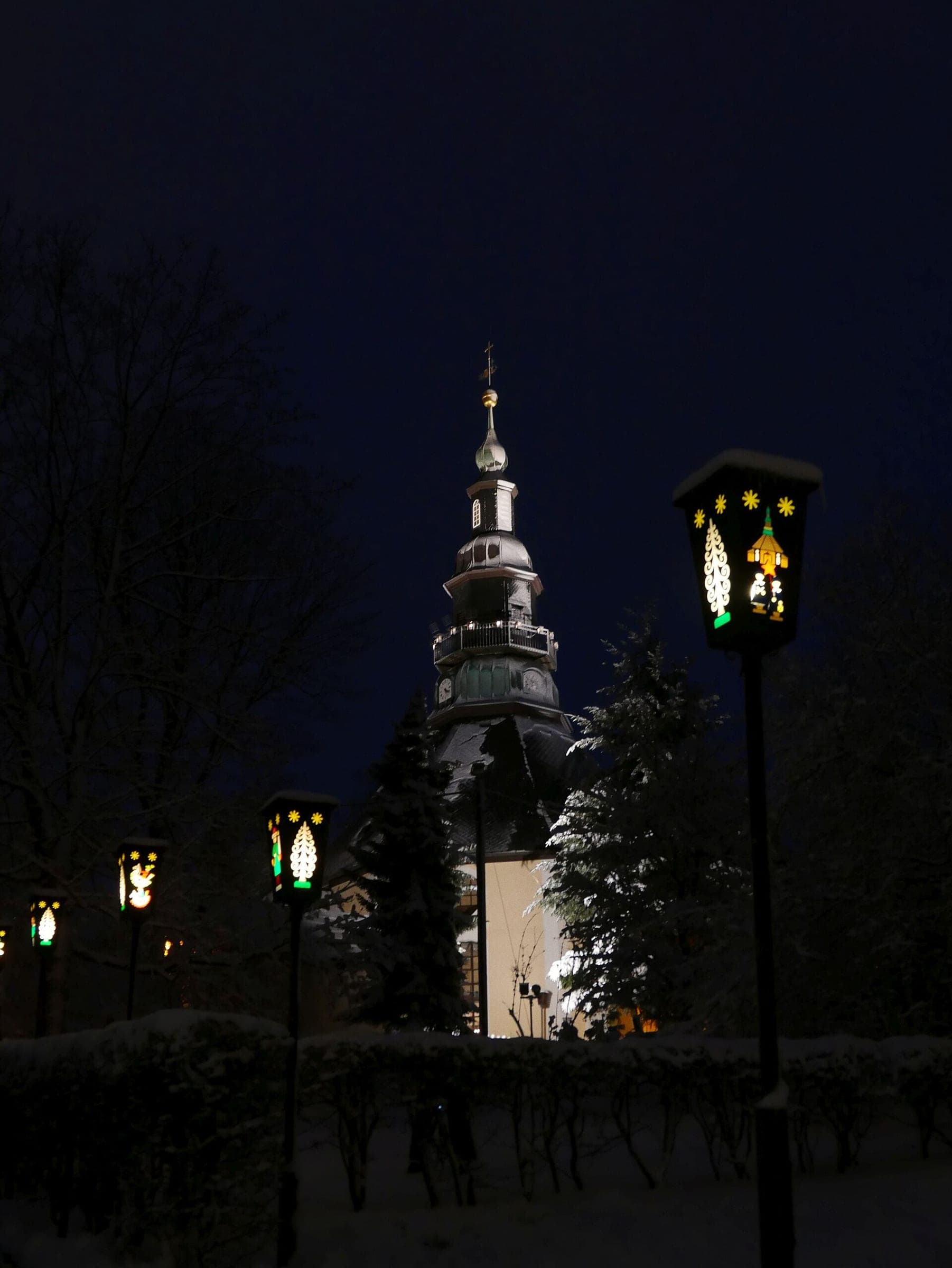 Painted Christmas lanterns light the path below the Bergkirche tower in Seiffen at night.