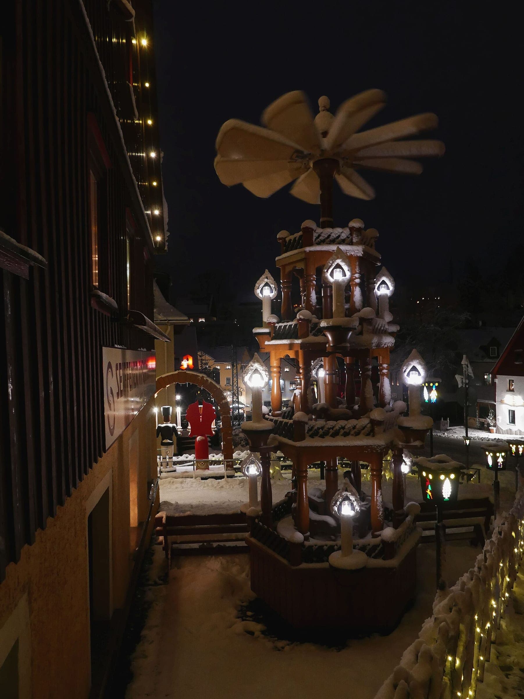 Lamps glow around a large Christmas pyramid on a snowy December night in Seiffen.