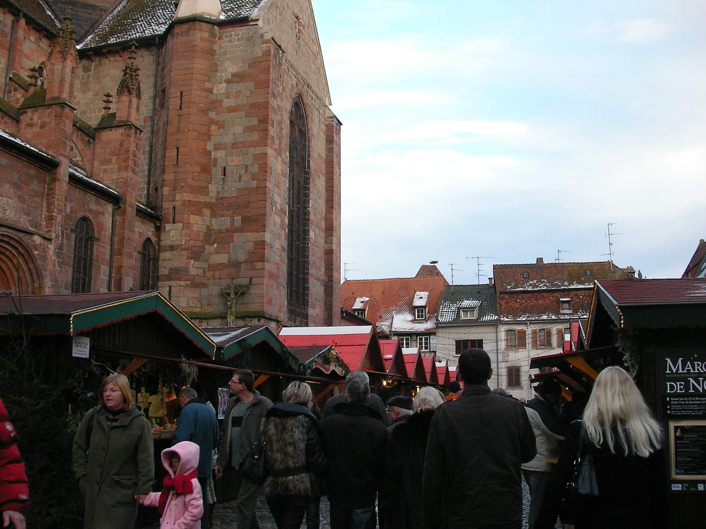 Shoppers browse red-roofed chalets beside the sandstone walls of Saint-Georges church in Sélestat.