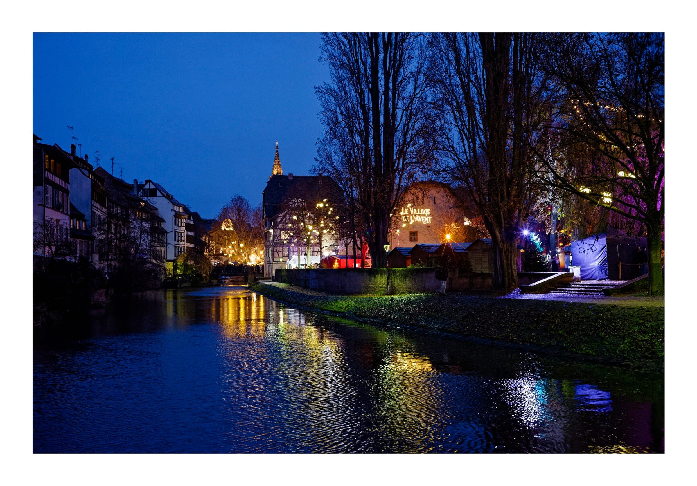 Lights from the Petite France market reflect in the Ill under a deep blue December sky in Strasbourg.
