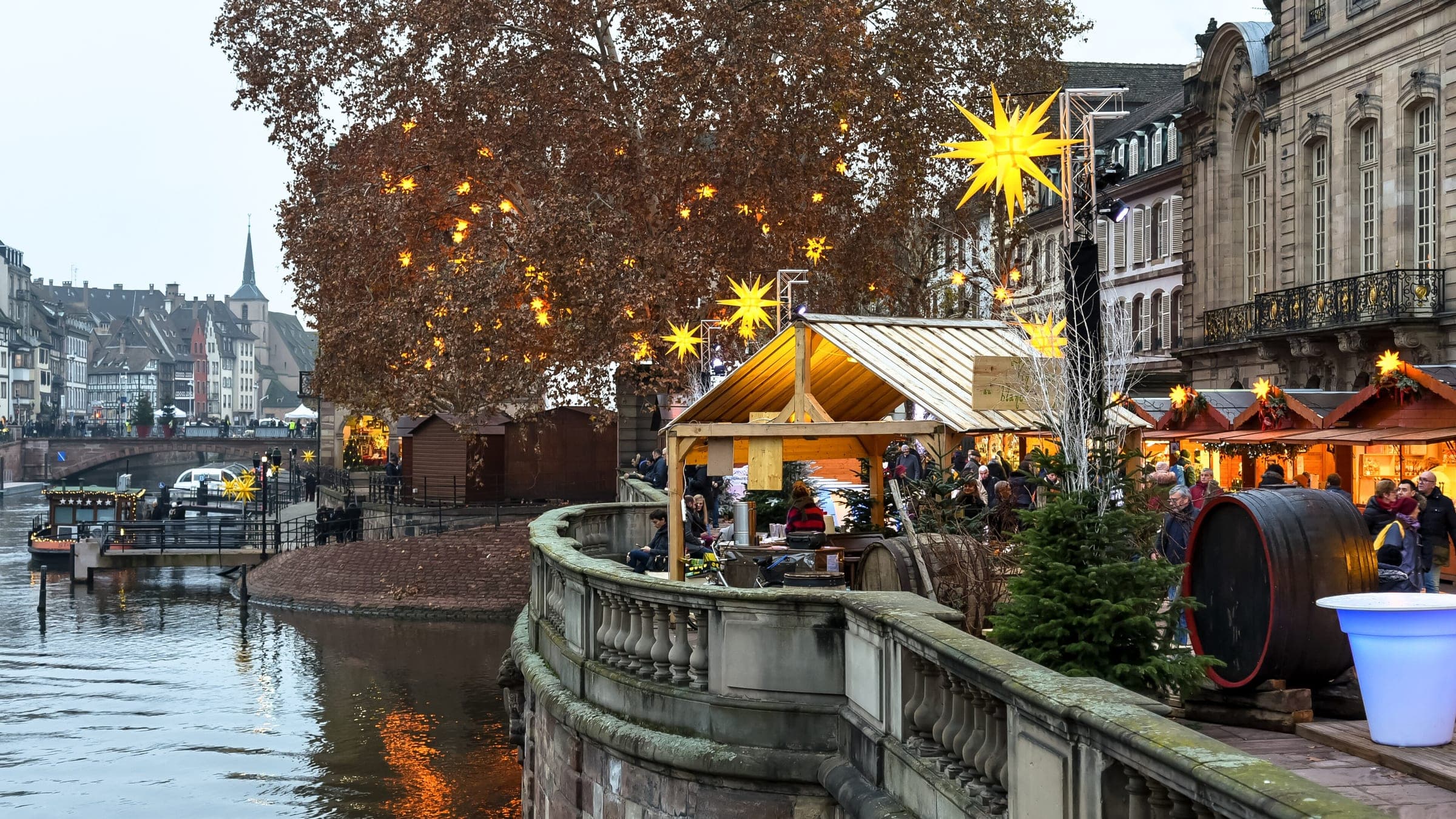 Lit stalls and a golden star line the Terrasse Rohan above the Ill in Strasbourg on a December afternoon.