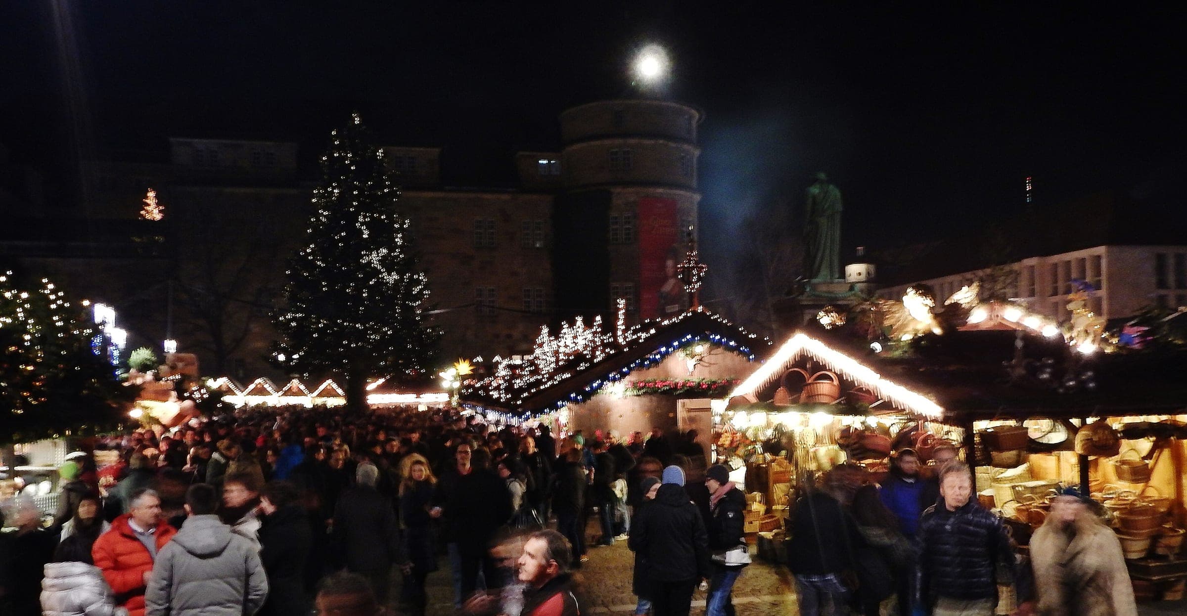 Crowds fill Stuttgart's Schillerplatz at night as the Christmas tree and stall roofs glow below the Altes Schloss.
