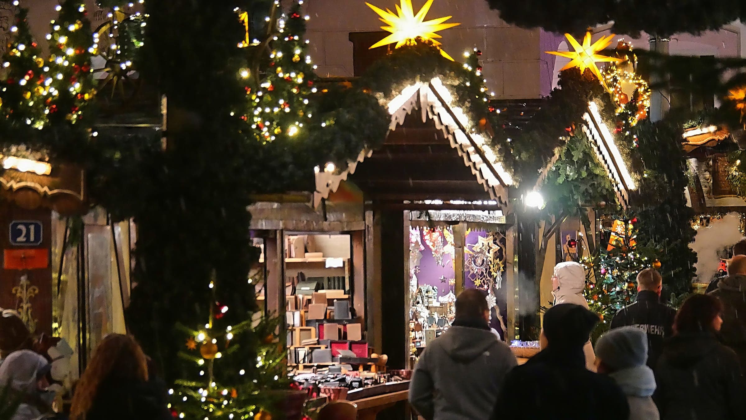 Paper stars and fir garlands hang over a lit gift hut at the Trier Christmas market at night