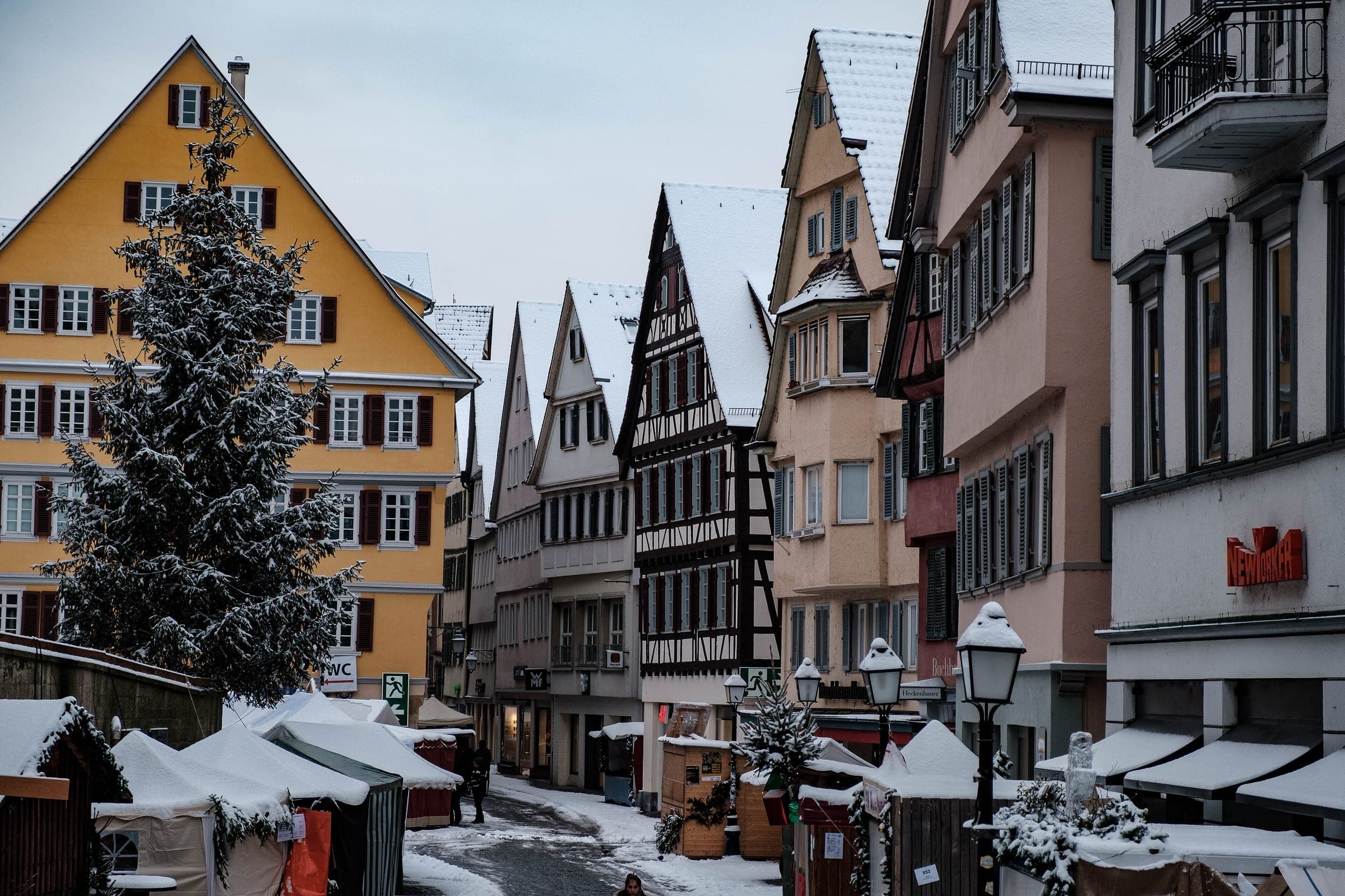 A snow-covered fir and white stall roofs line the lane by the Stiftskirche during Tübingen's Christmas market.